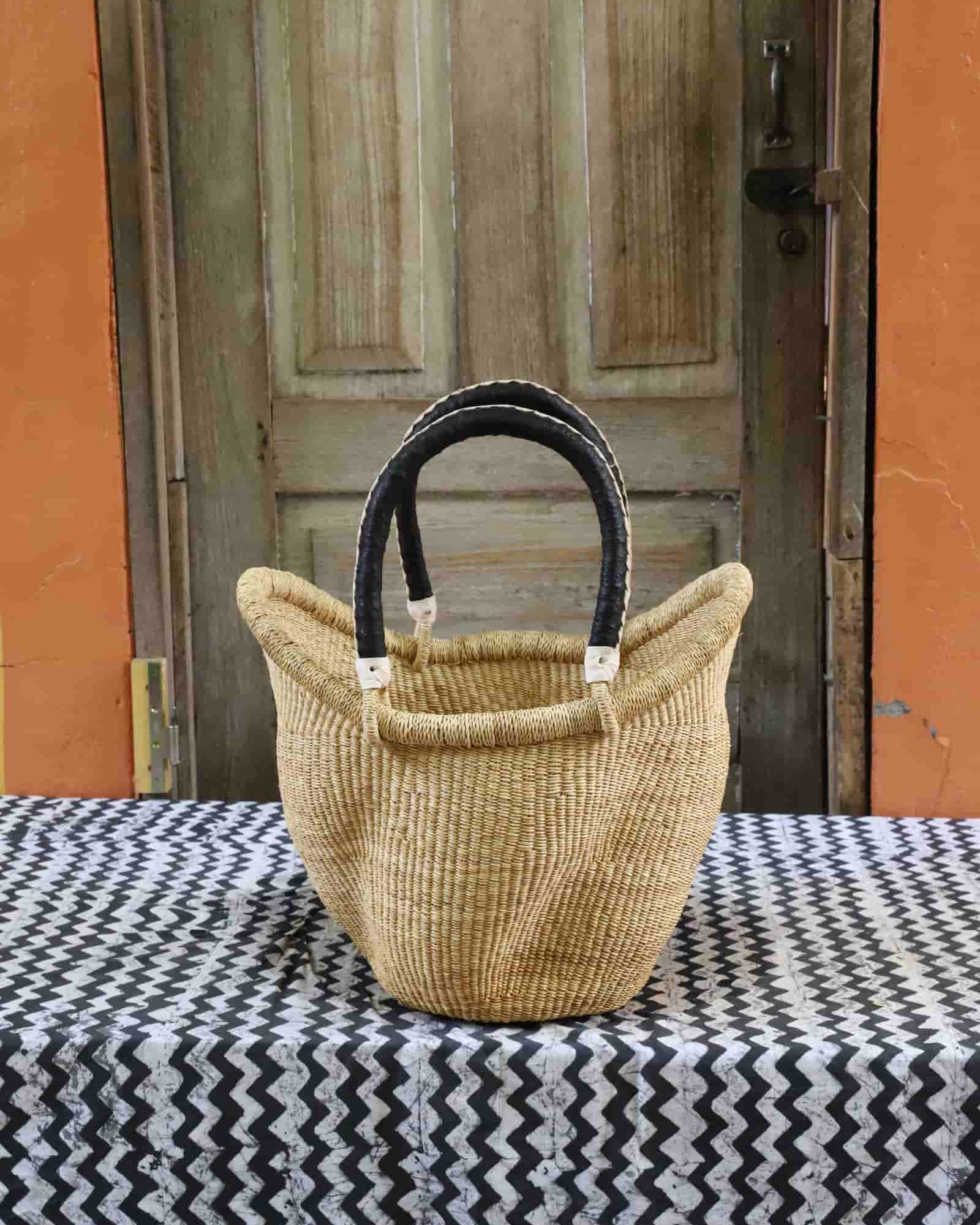 Woven basket with black handles on a tablecloth in front of a wooden door.