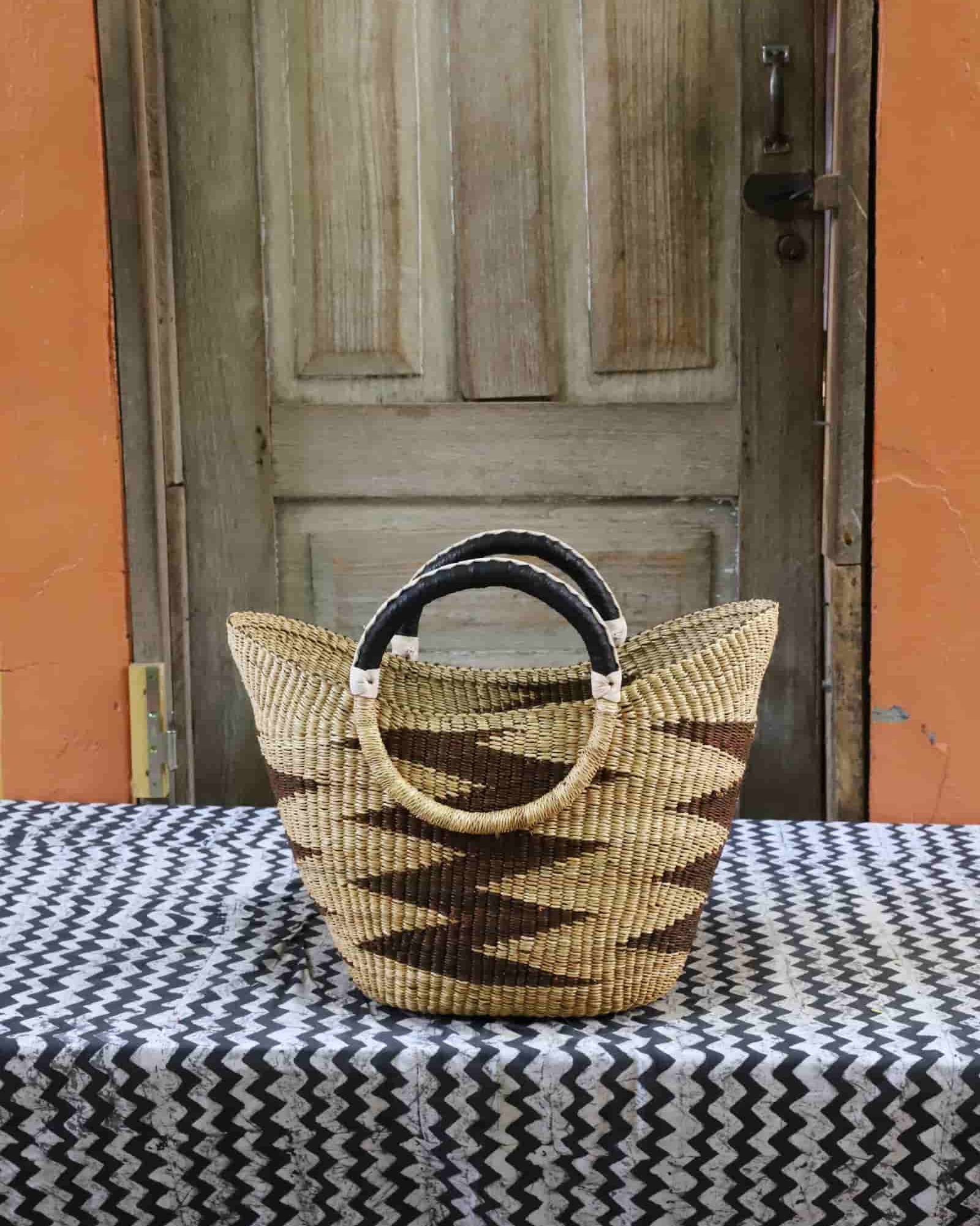 Woven basket with black and beige handle on a tablecloth in front of a wooden door.
