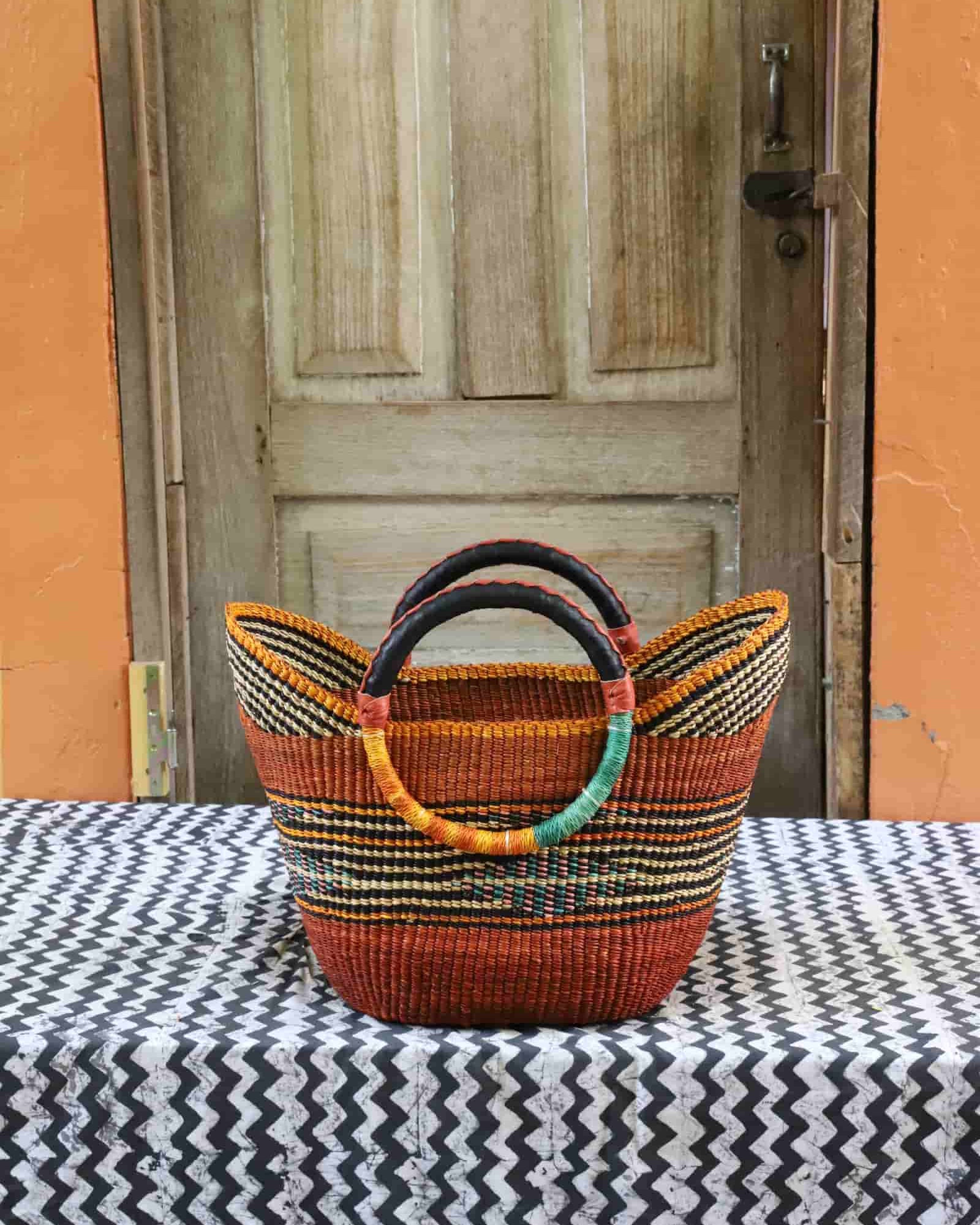 Woven basket with colorful handles on a tablecloth in front of a wooden door.