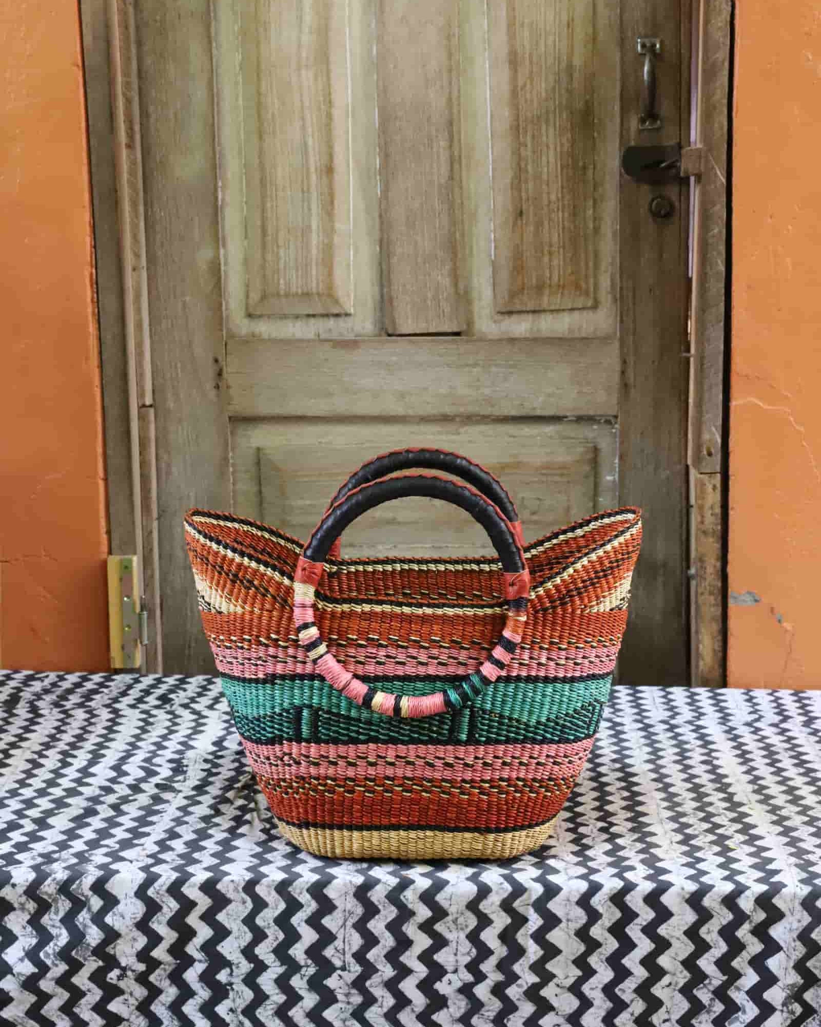 Woven basket with colorful pattern on a table in front of a wooden door.