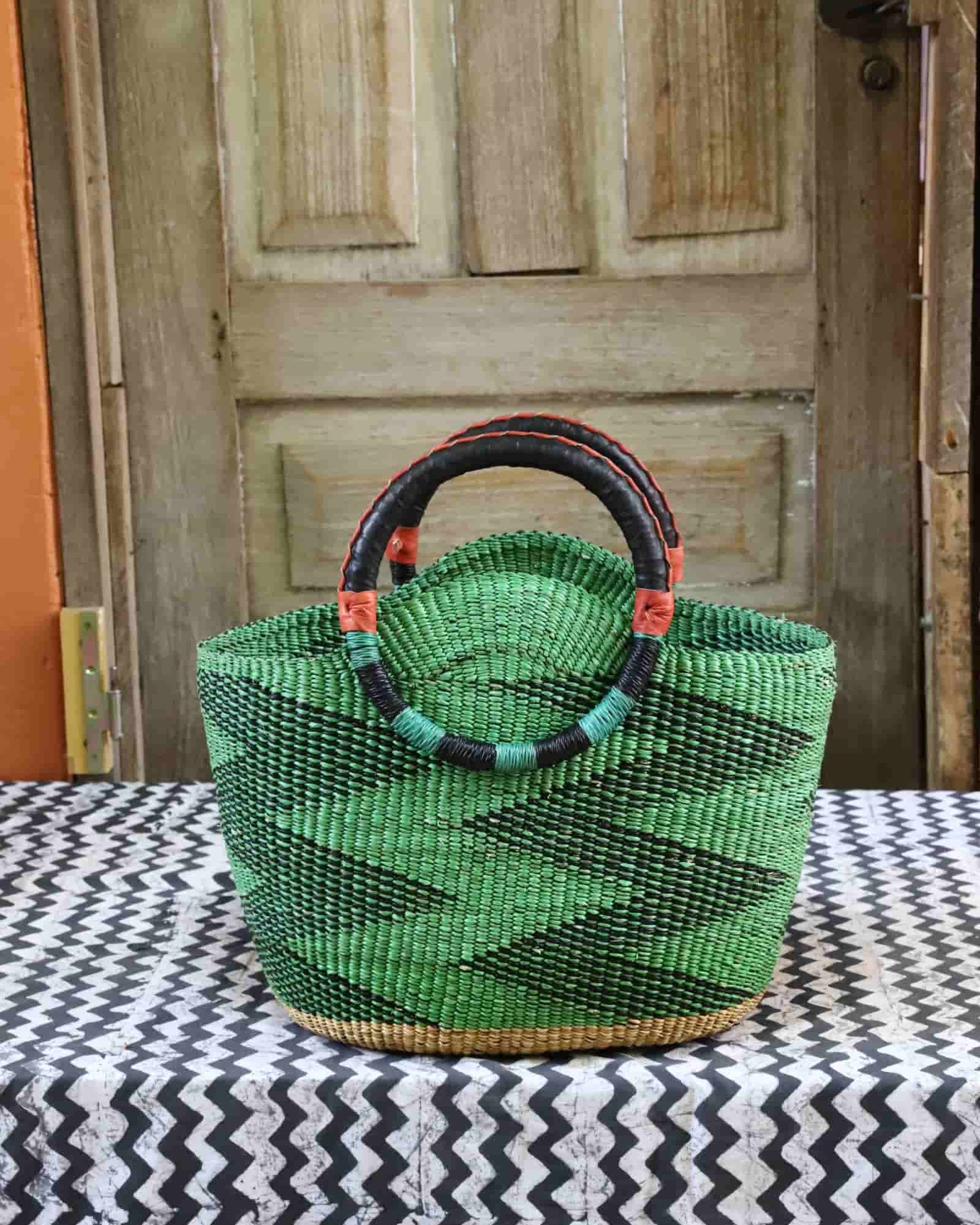 Green woven basket with black handle on a tablecloth in front of a wooden door.
