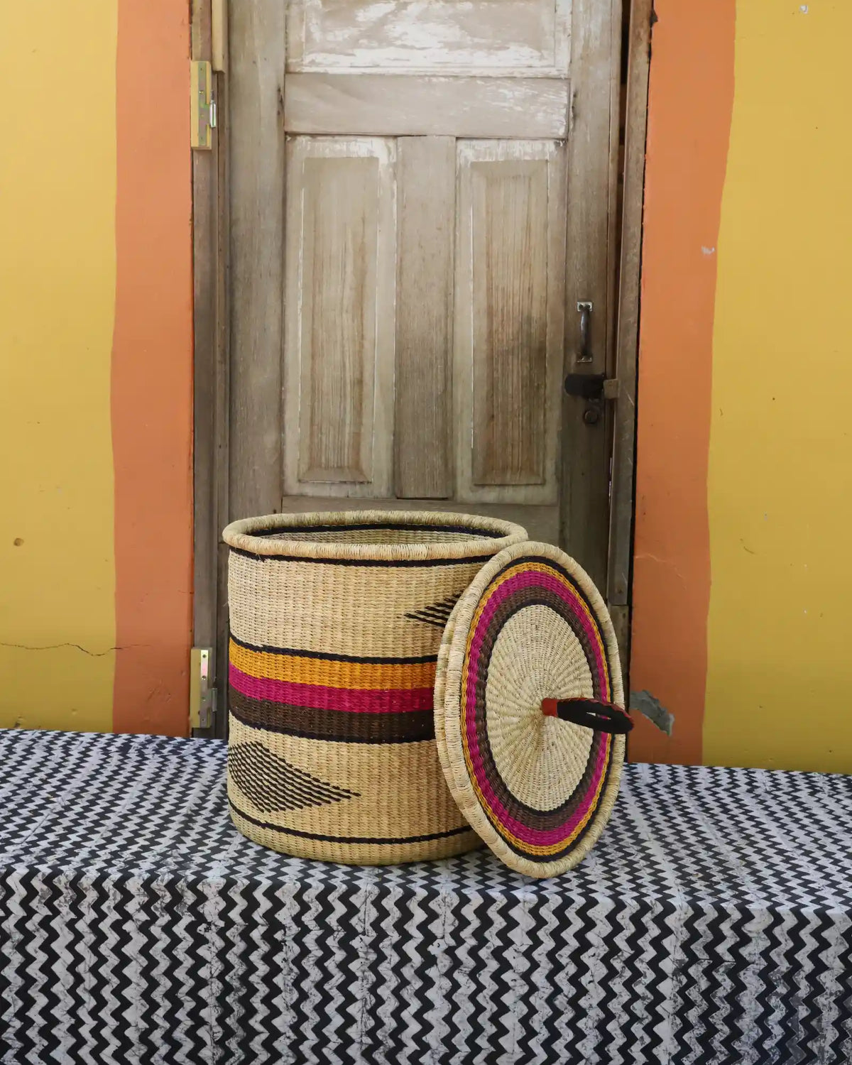 Handwoven Bolga laundry basket with lid removed, natural body with pink and orange bands and matching lid.
