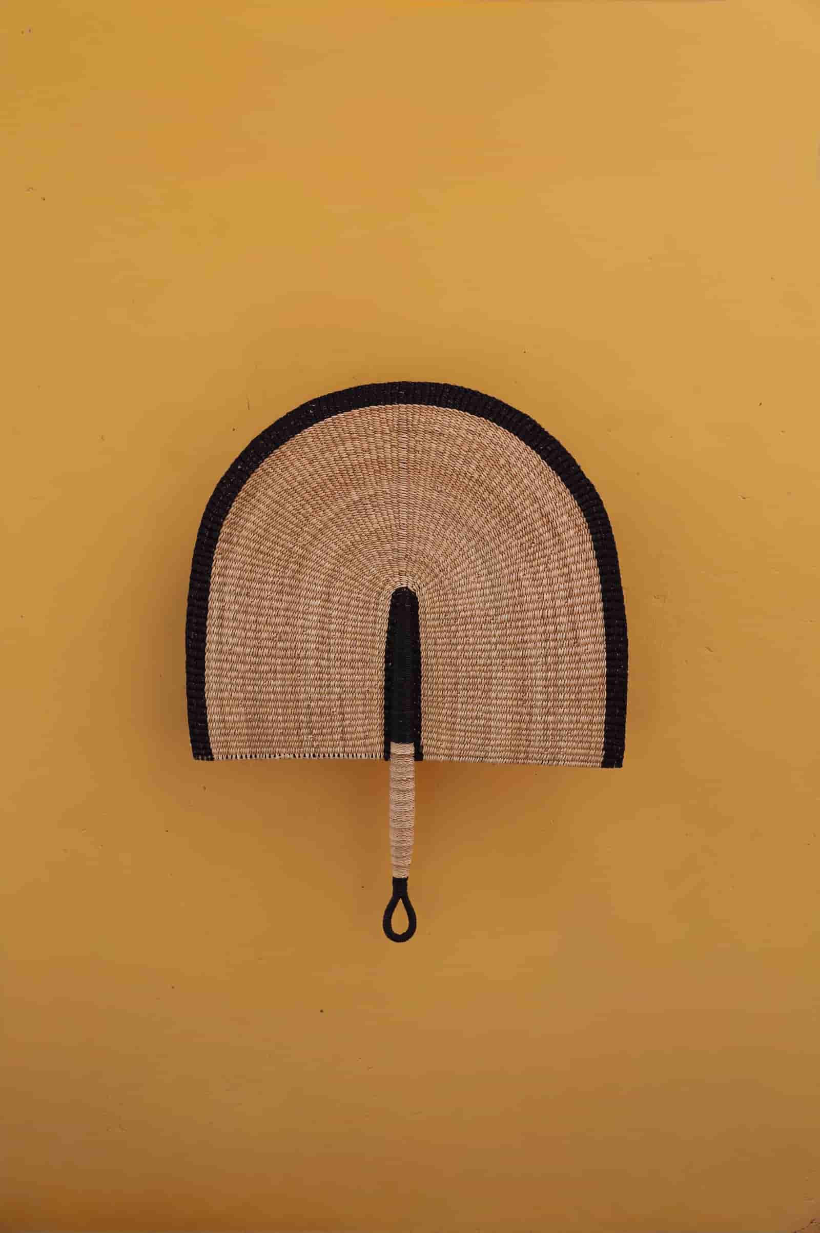 Woven hand fan with black rim on a yellow background