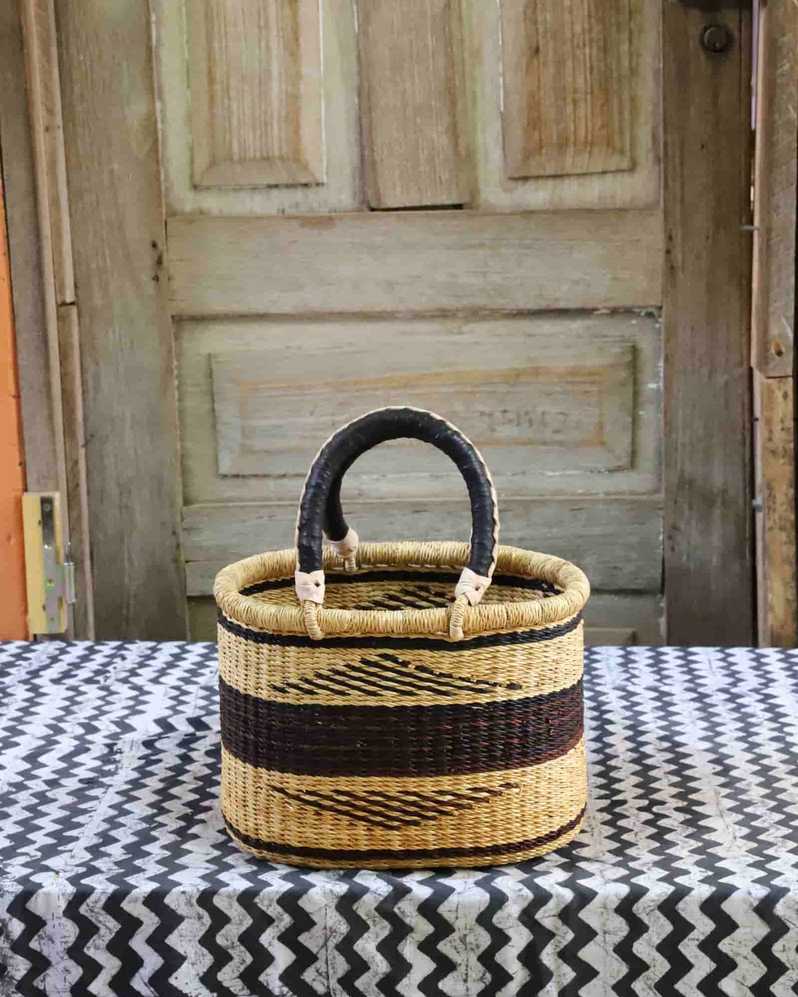 Woven basket with black handle on a patterned tablecloth in front of a wooden door.