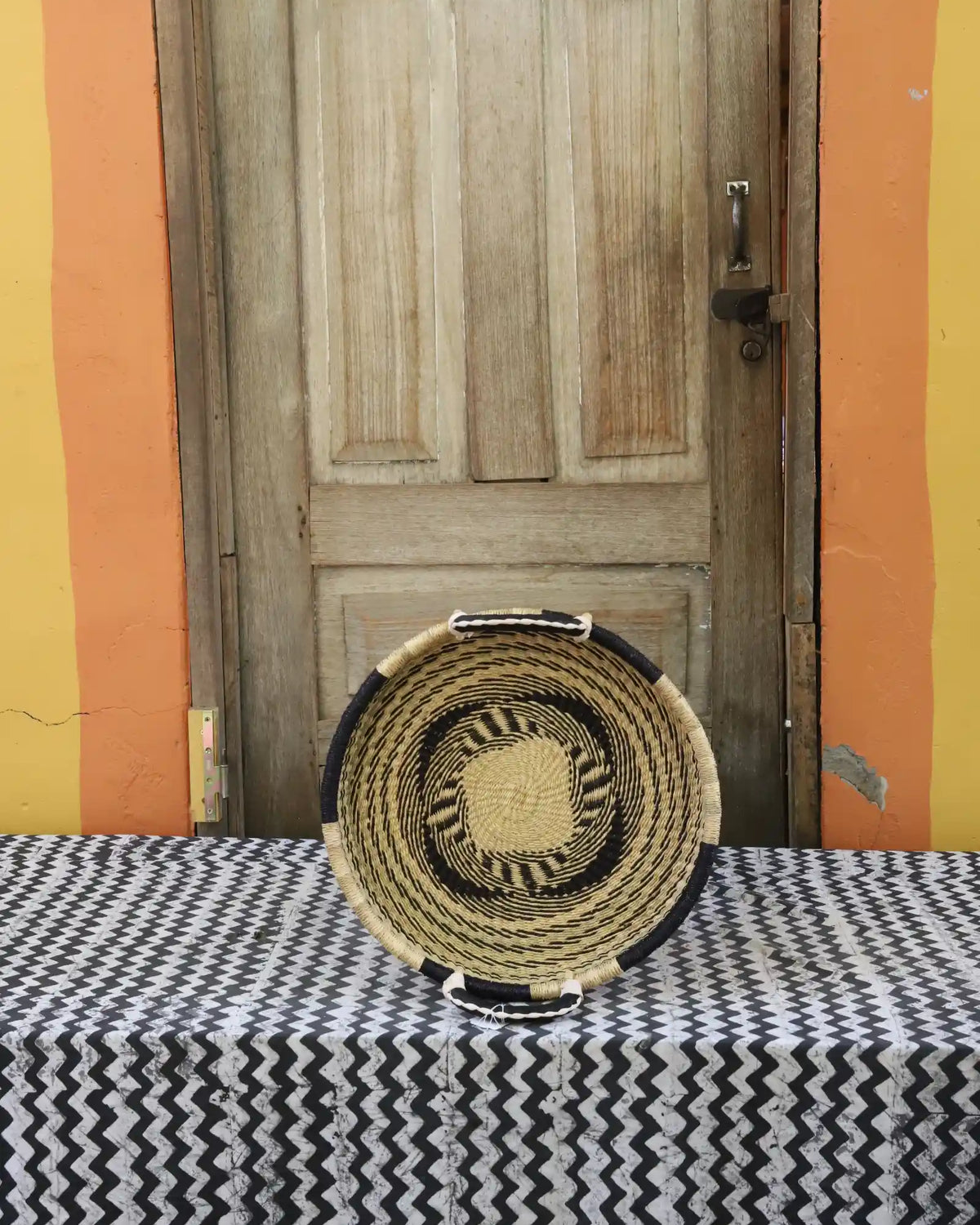 Handwoven Bolga wall tray disc in natural straw with a dark rim and yellow centre dot.
