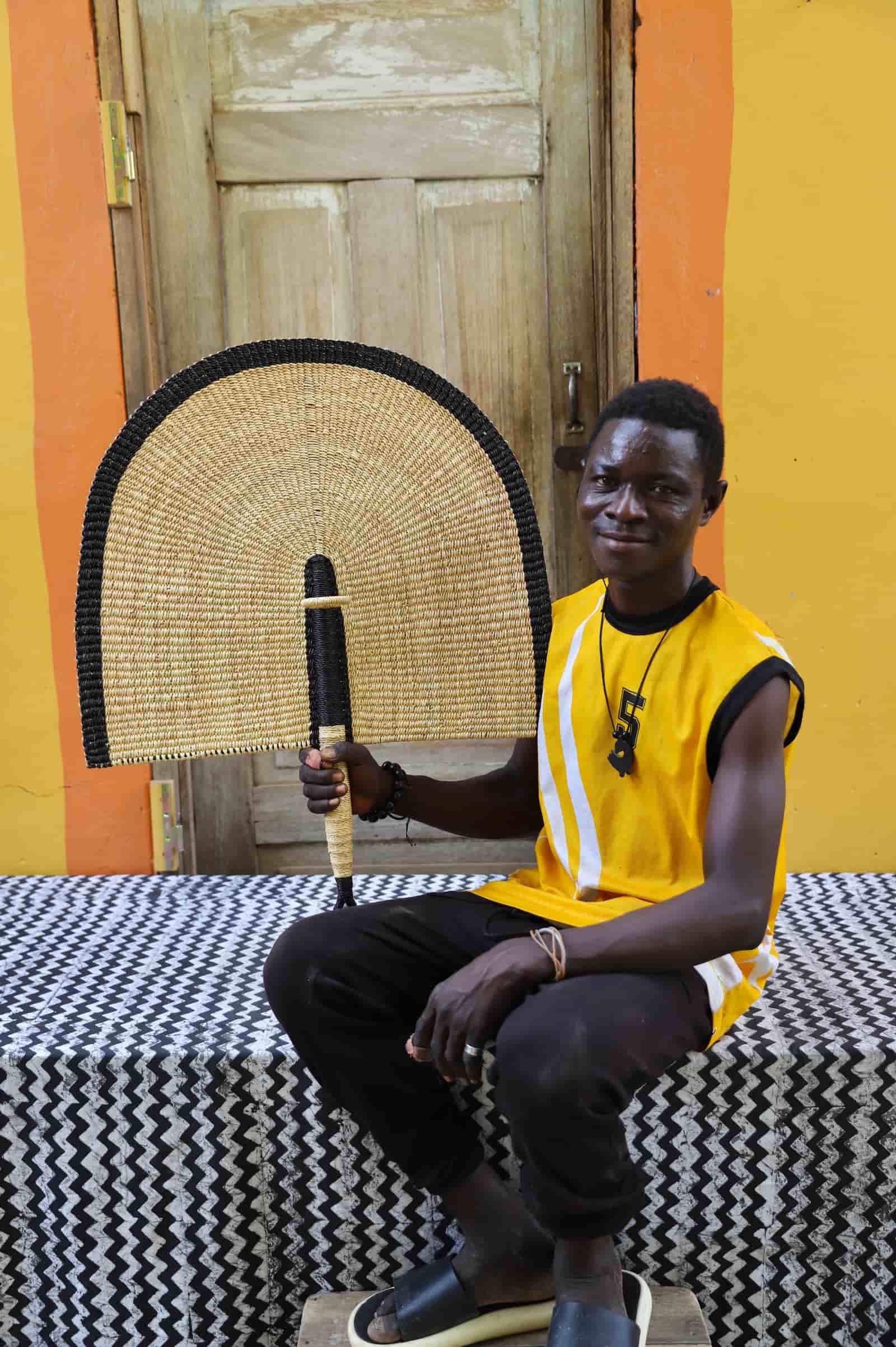 Man holding a traditional woven object against a colorful wall.