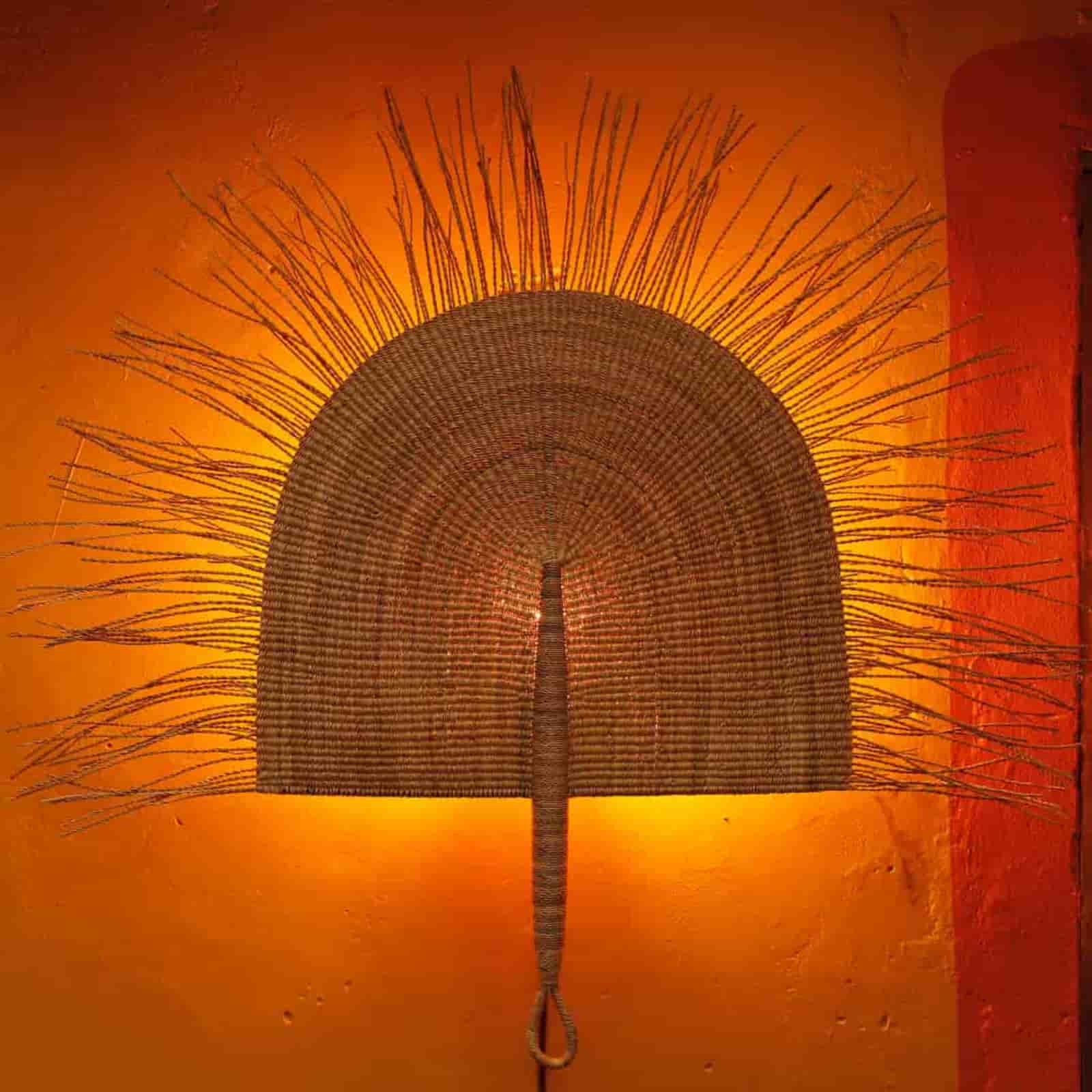 Woven wall art with a sunburst design on an orange wall