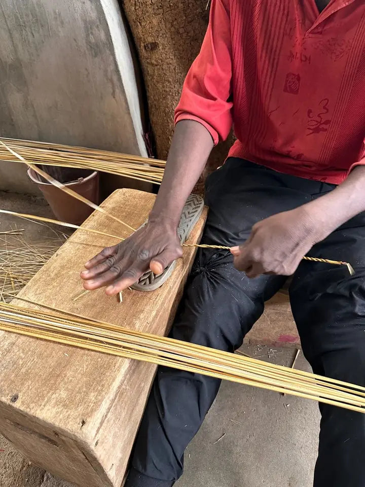 A basket maker preparing long strands of straw on a wooden bench