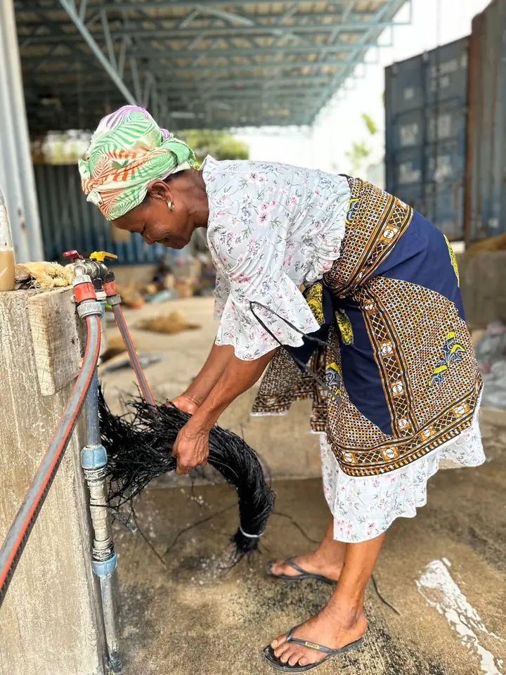 A basket maker rinsing prepared straw beside a bucket