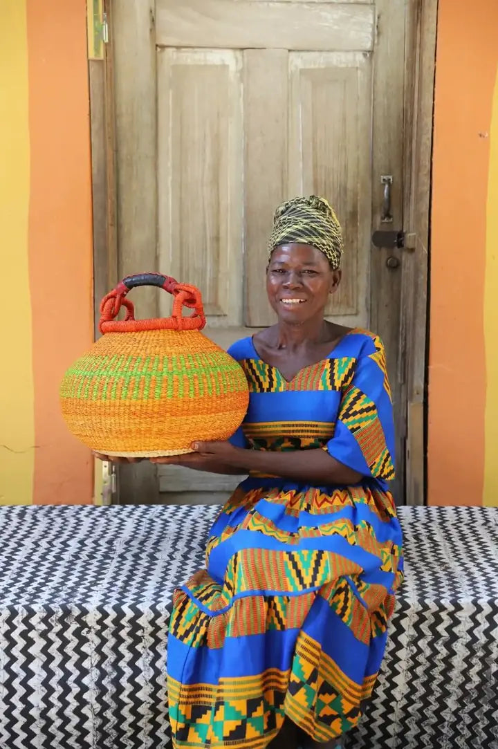 A basket maker seated with a finished basket with orange and green bands