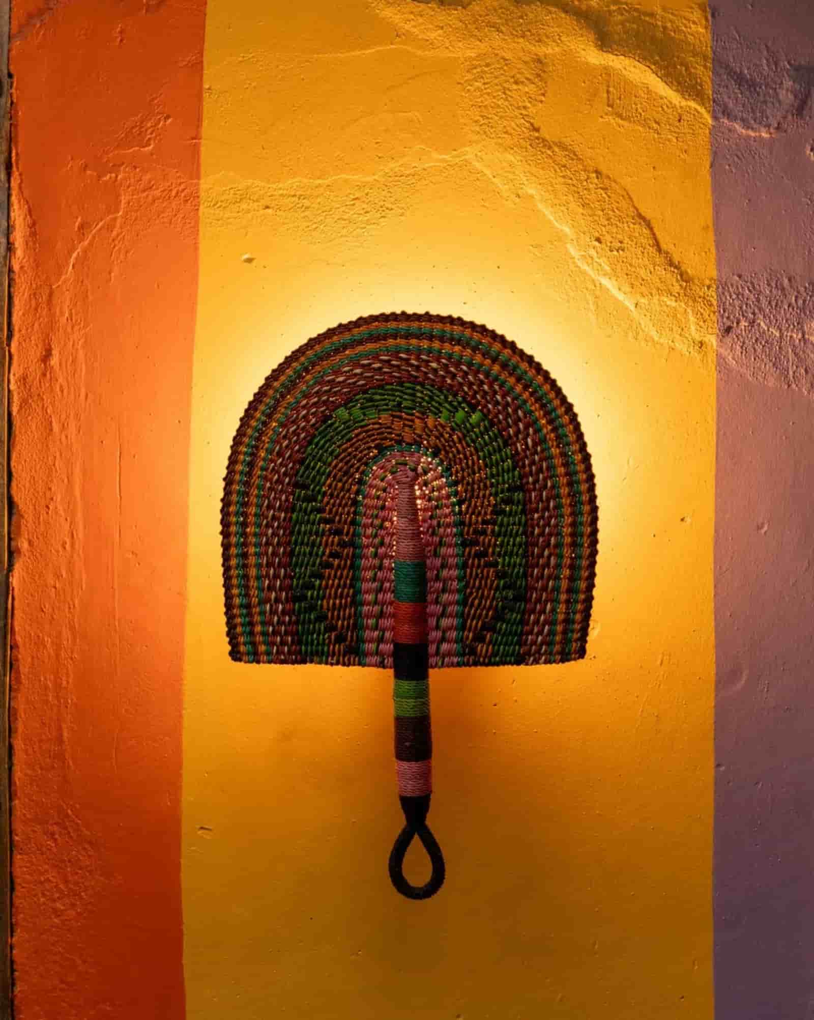 Colorful woven wall art against a textured wall with warm lighting