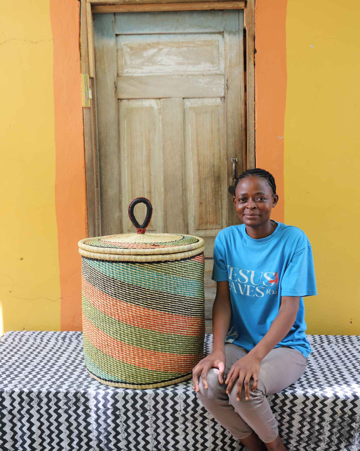 Handwoven Bolga laundry basket with fine multicolour diagonal stripes, beside a seated woman in blue.