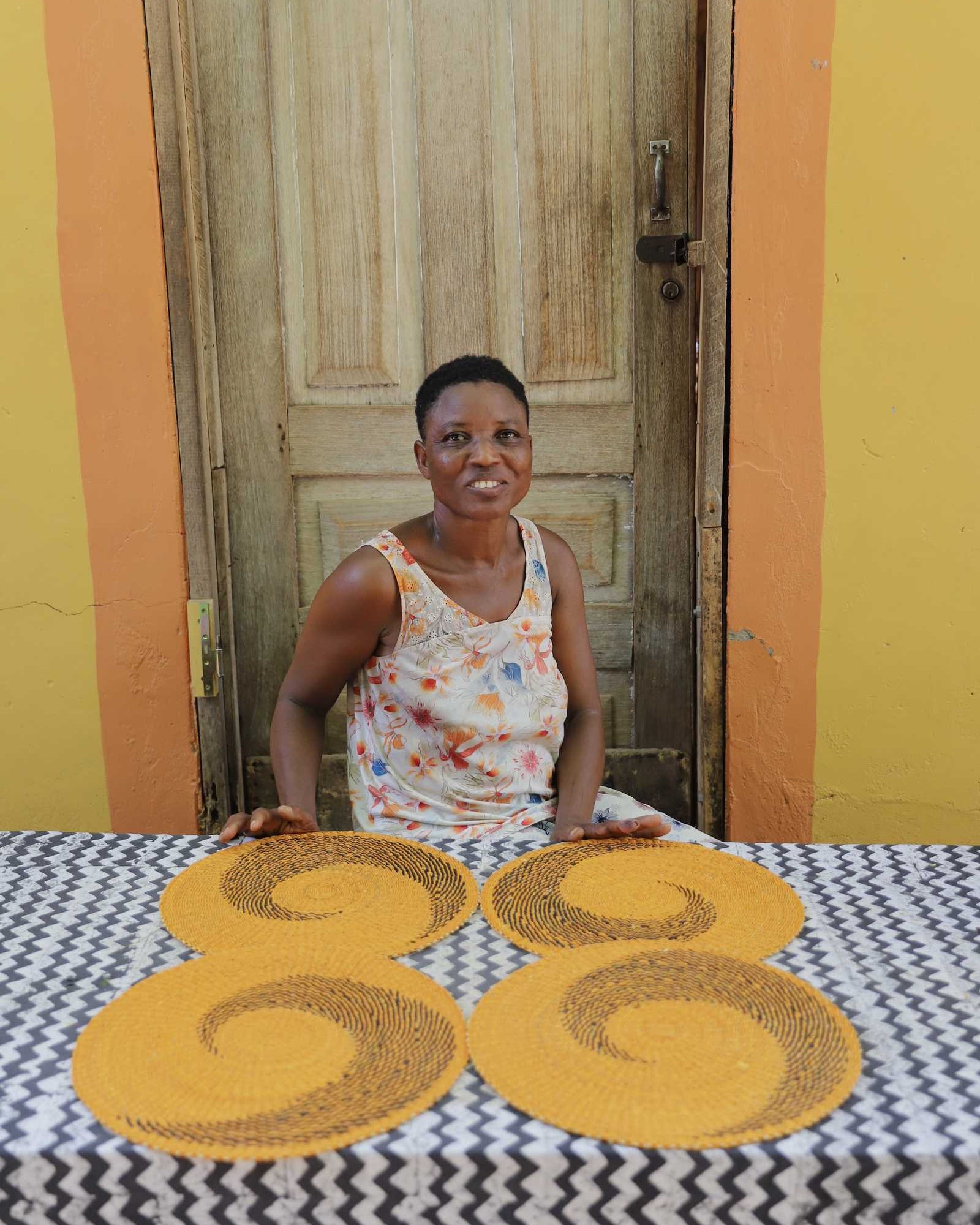Two handwoven Bolga placemats in natural straw with black spiral pattern, displayed by their maker in Bolgatanga, Ghana.