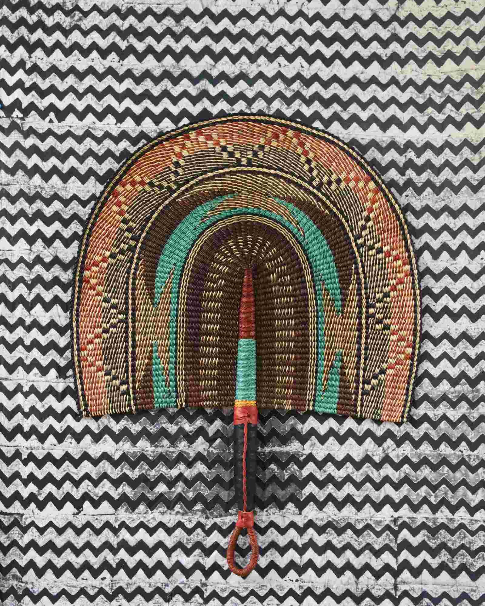 Naba Penga wall fan in natural straw with a teal arch and orange patterned border, laid on a chevron cloth.