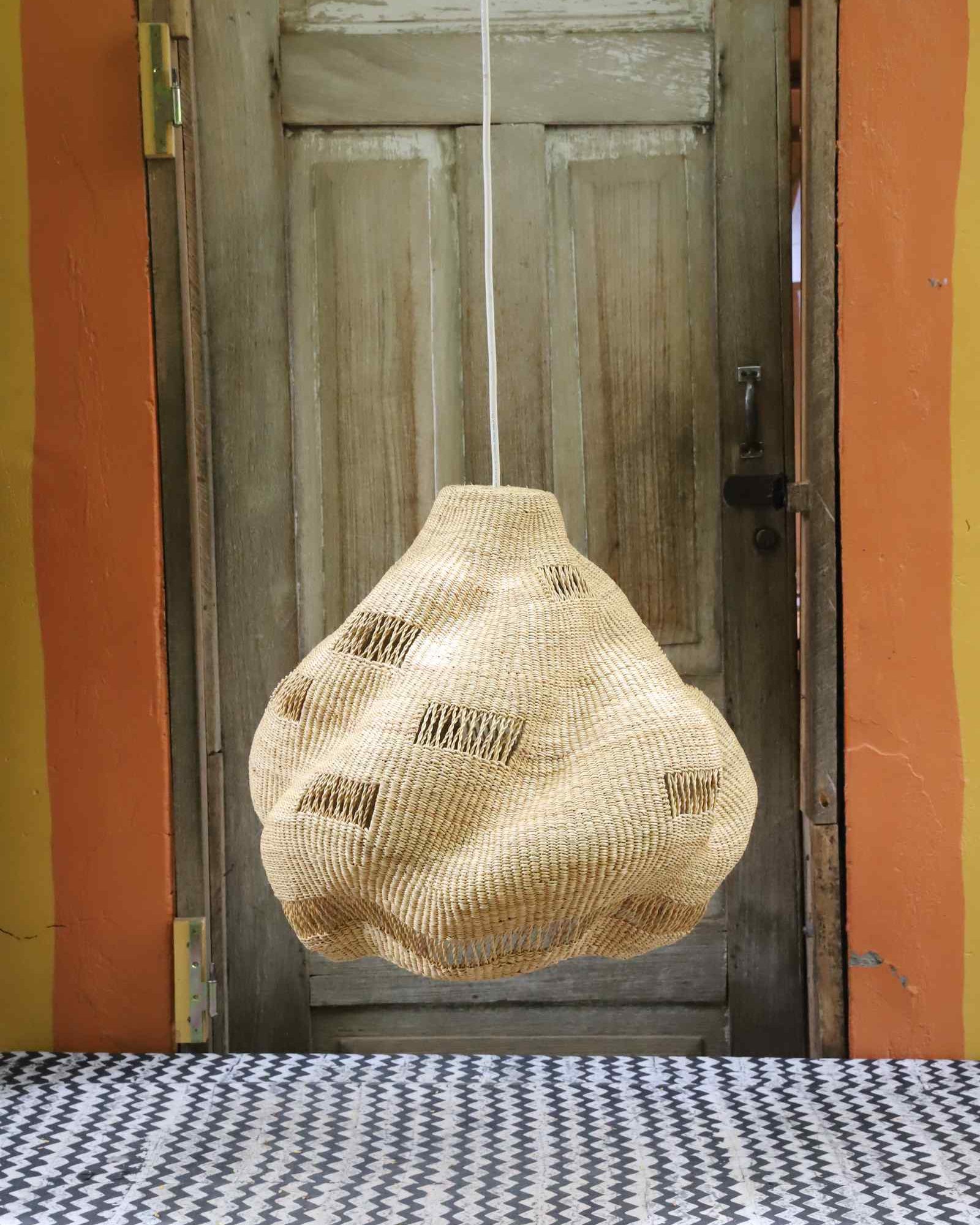 Cosma pendant lampshade in woven elephant grass with dotted light openings, hung against a weathered door.