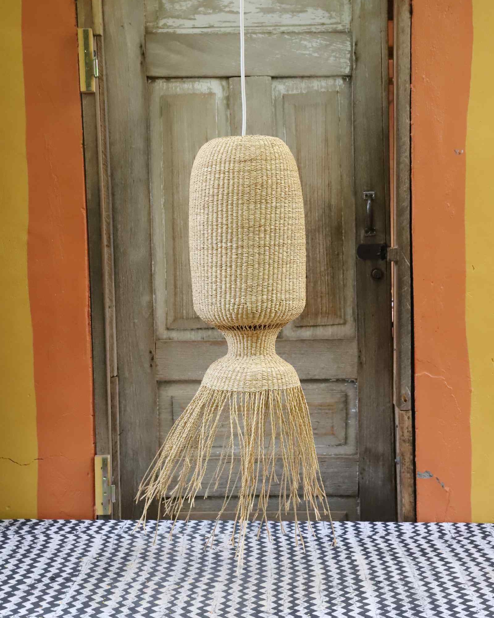 Elephant grass Abyssal pendant lampshade with tapered fringe base, hung against a weathered door.