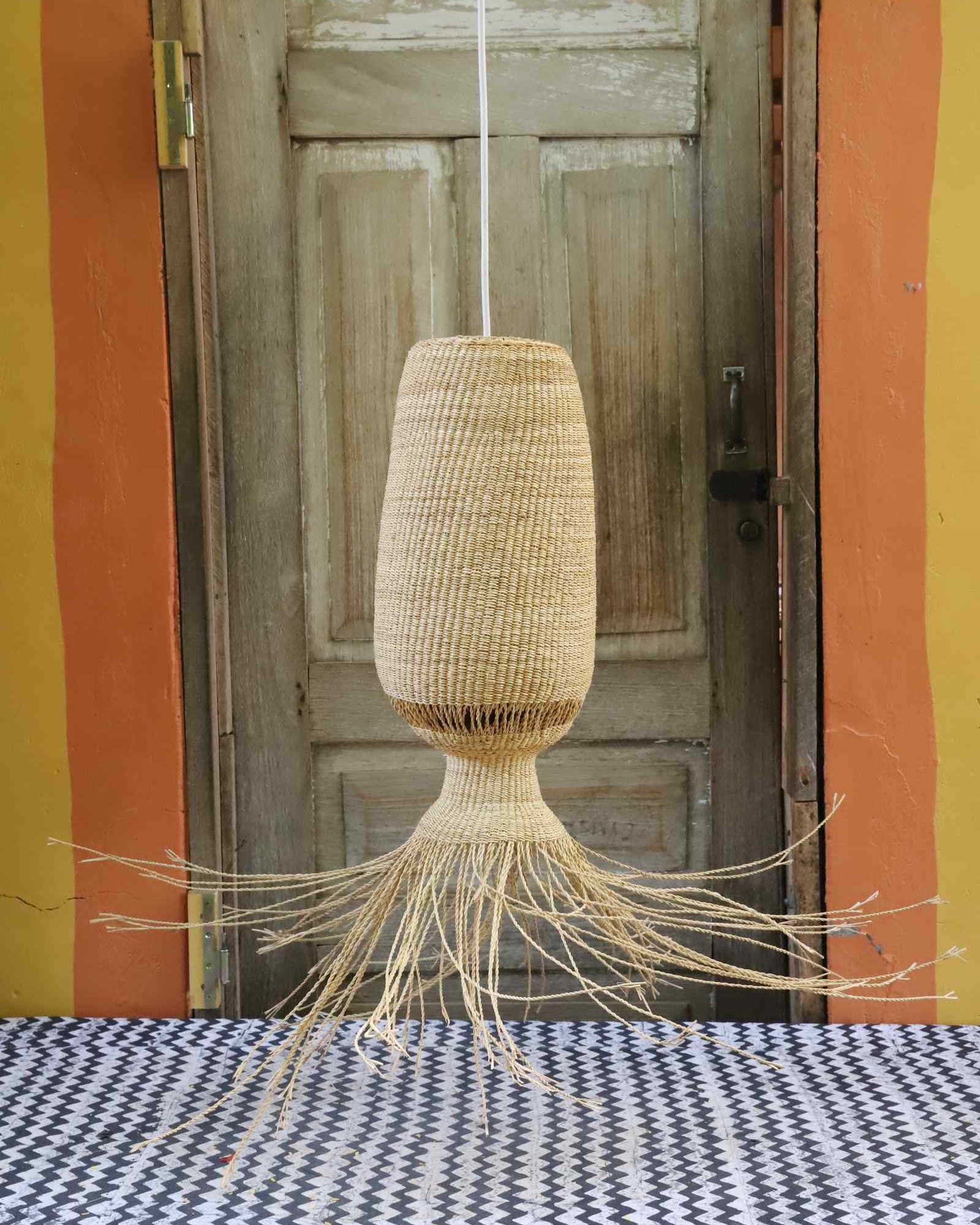 Abyssal pendant lampshade with long trailing fringe, hanging before a weathered wooden door.