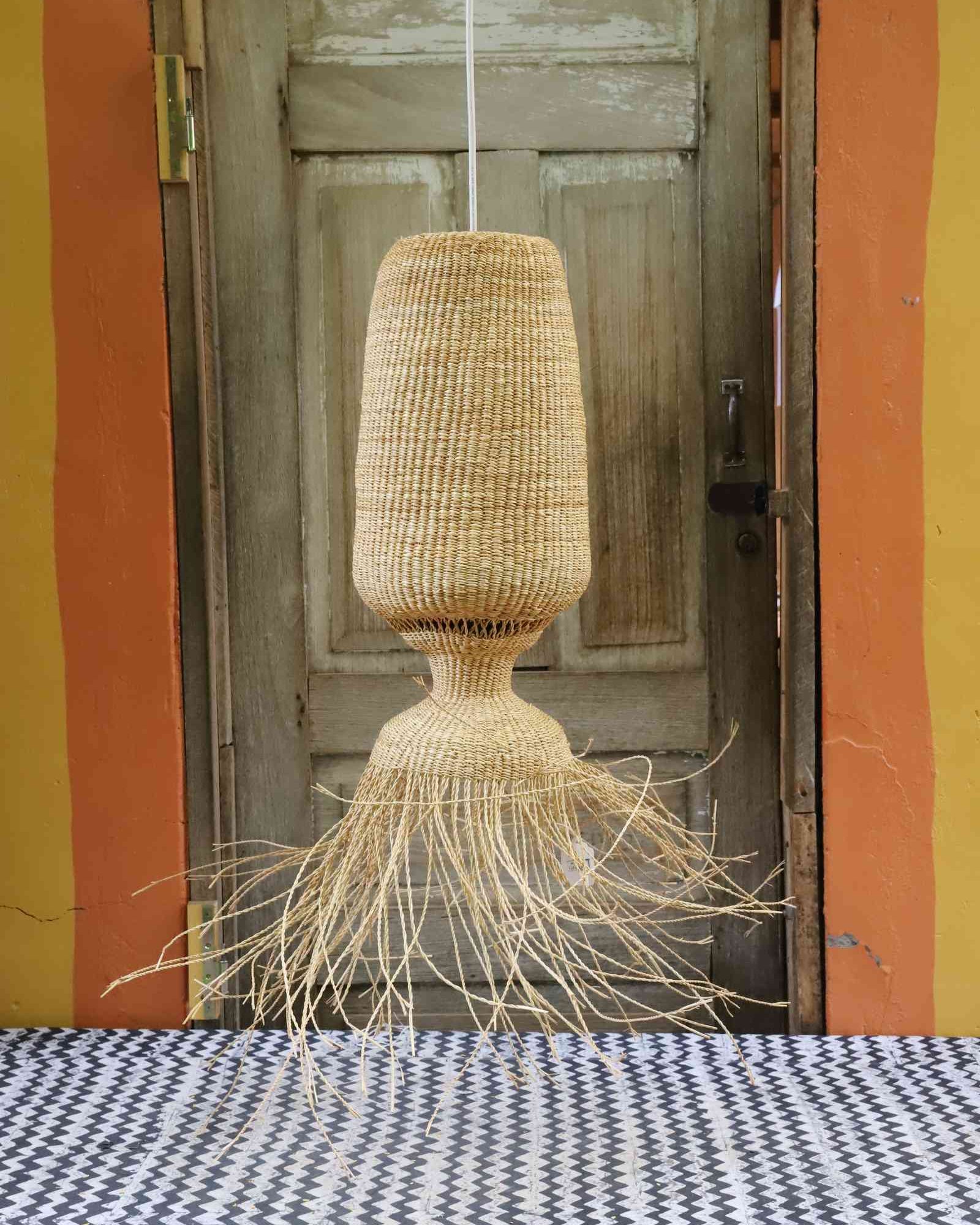 Abyssal pendant lampshade with a wide fringed base, hanging in front of a weathered wooden door.