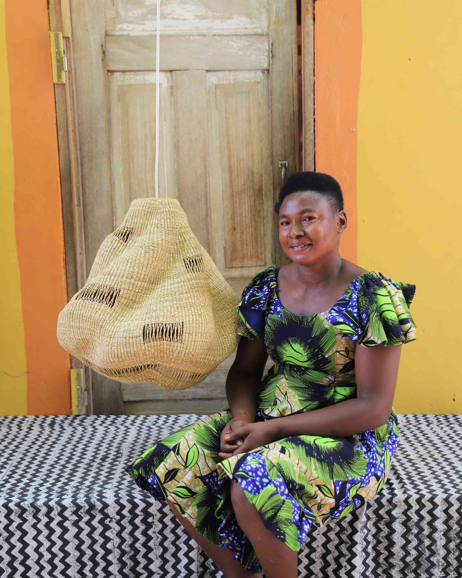 Woman in a floral dress seated beside the Cosma pendant lampshade in a weathered doorway.