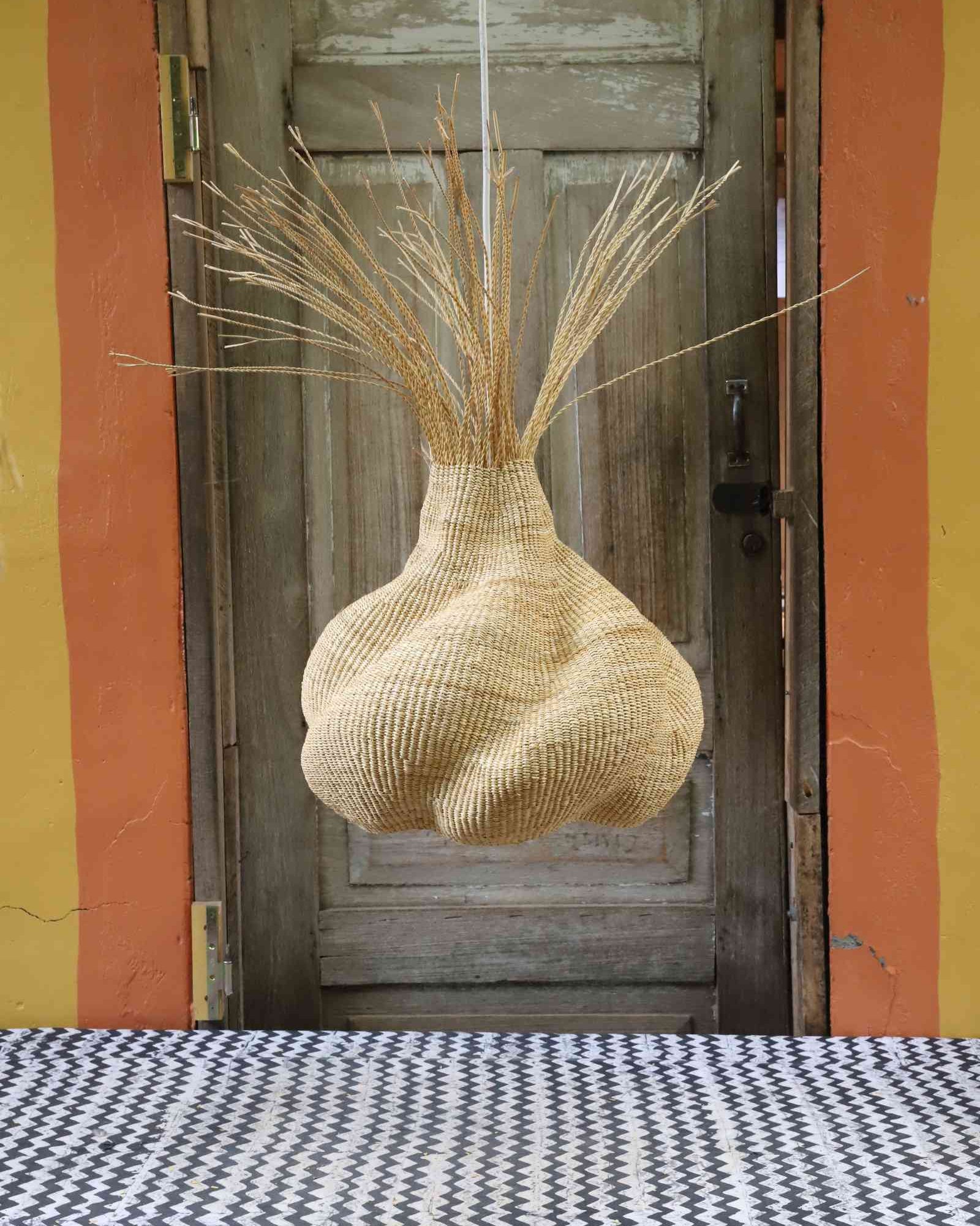 Rounded Helix pendant lampshade with a fanned straw fringe, hanging before a weathered wooden door.