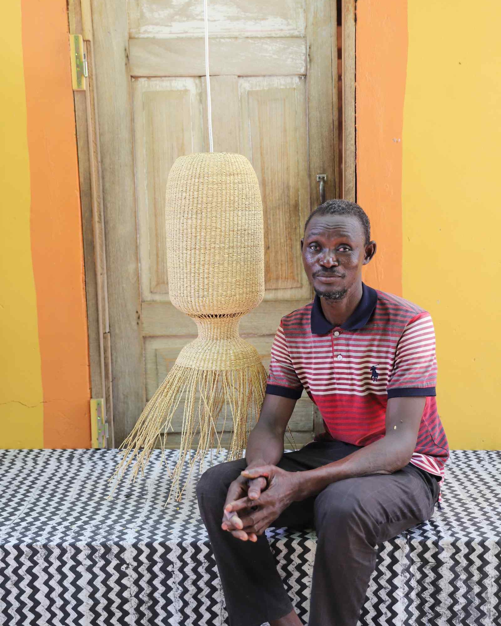 Man seated on a woven bench beside the Abyssal lampshade in a weathered doorway.