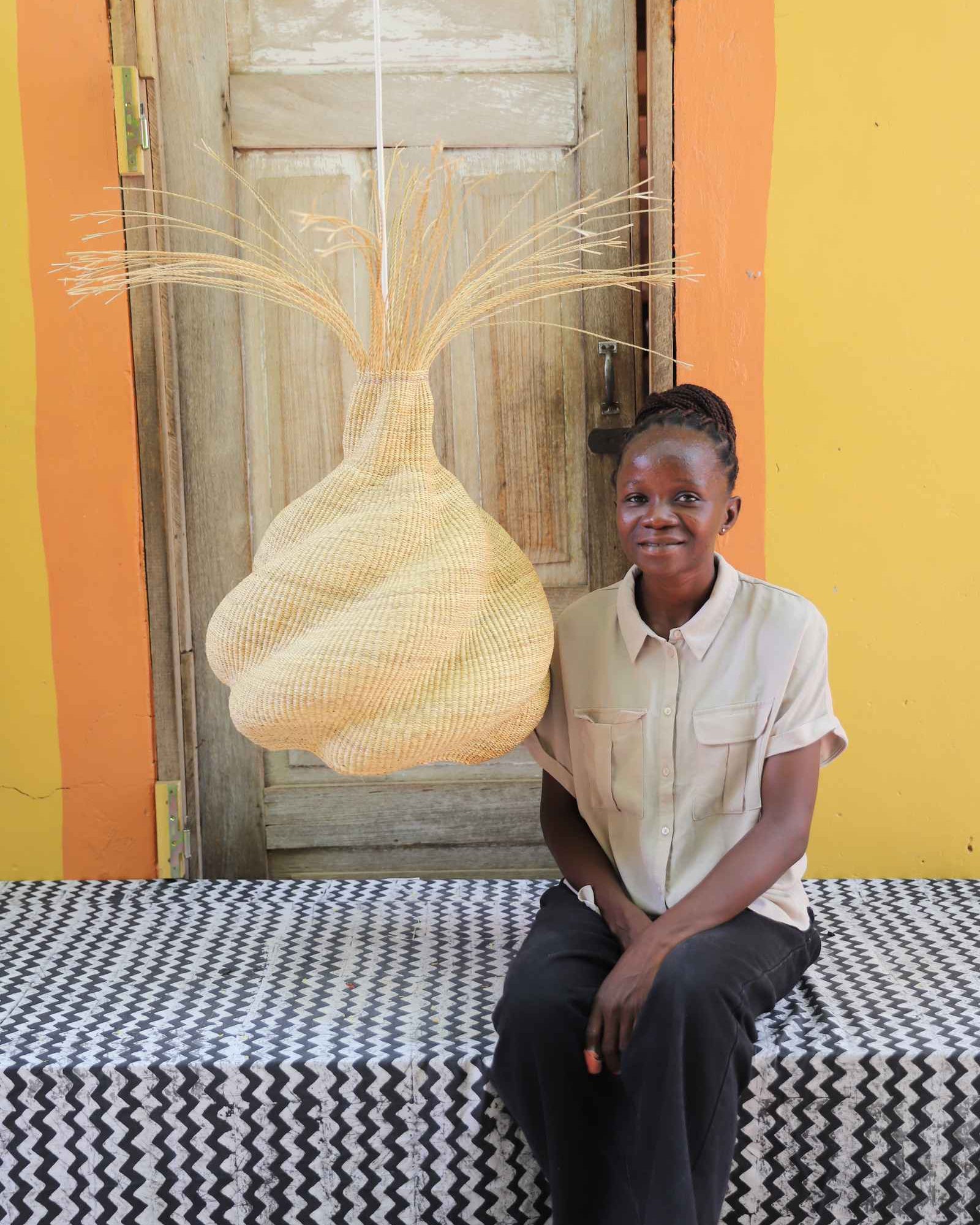 Boy seated on a woven bench beneath the Helix pendant lampshade in a weathered doorway.