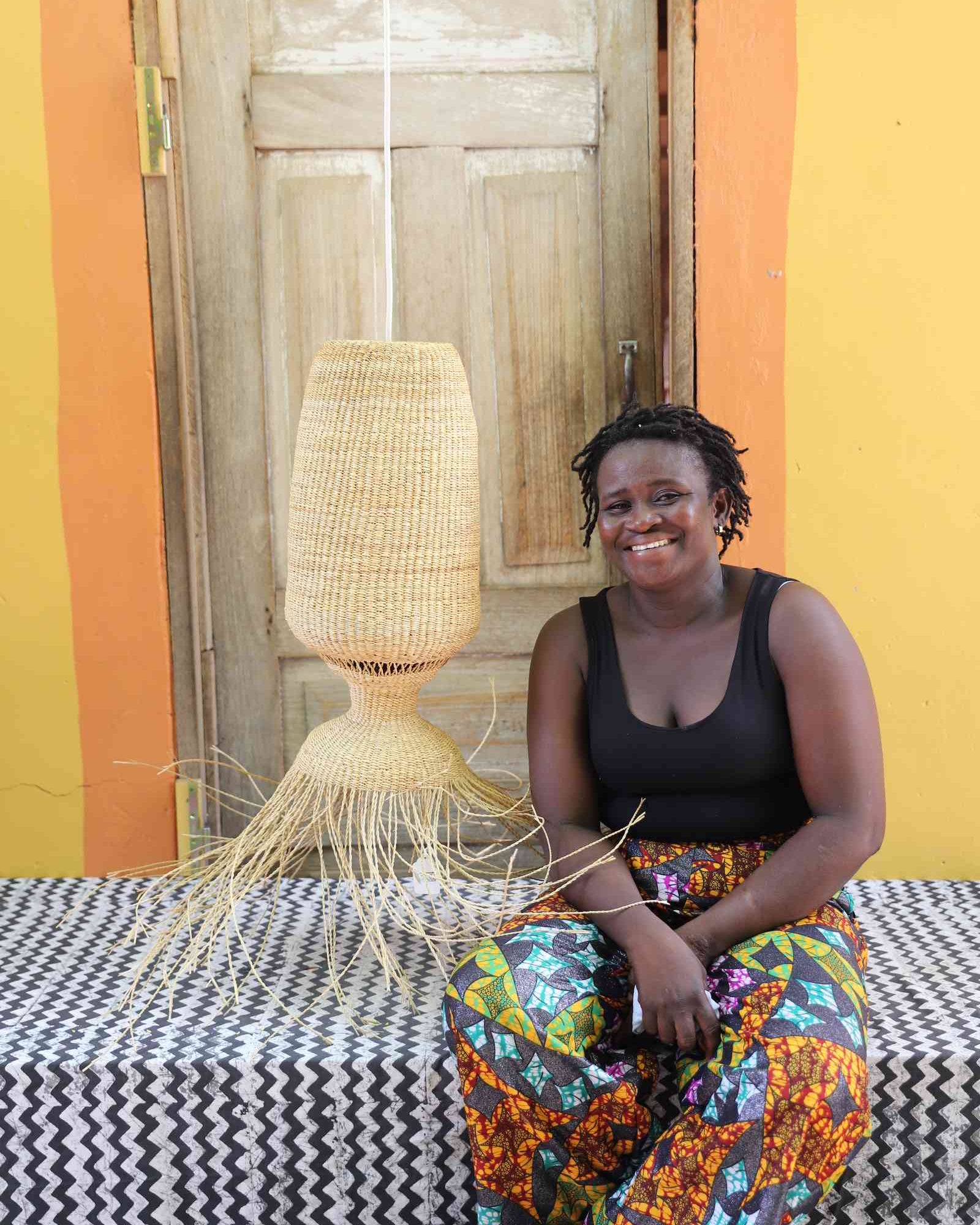 Woman seated on a woven bench beside the Abyssal lampshade in a weathered doorway.