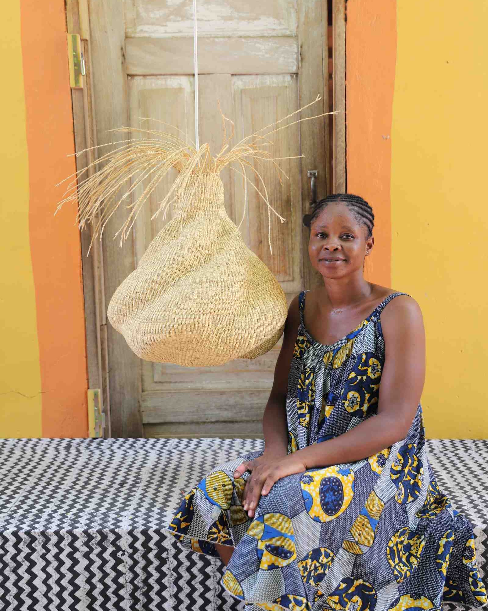 Woman in a floral dress seated beside the Helix pendant lampshade in a weathered doorway.