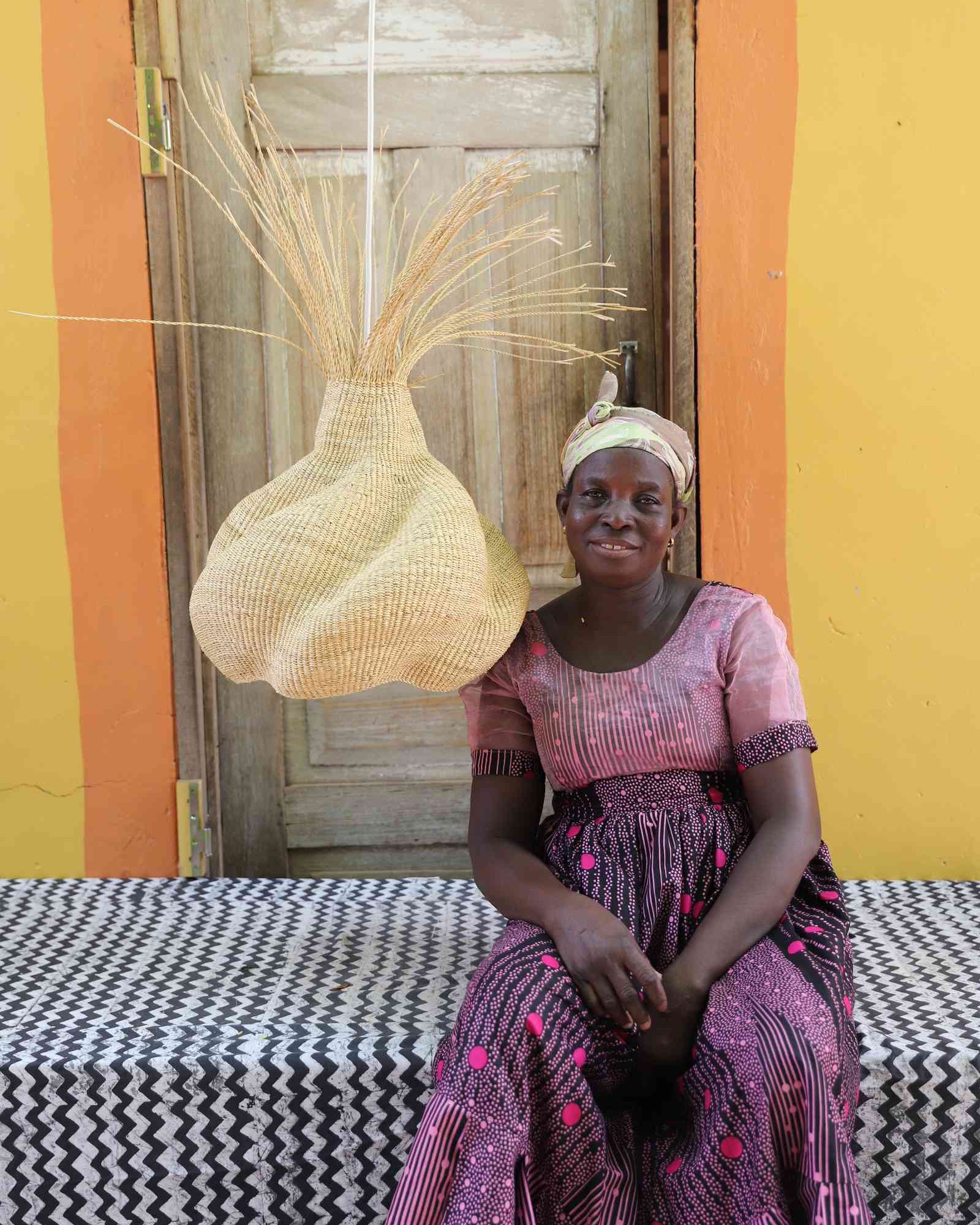 Woman in a pink dress and headwrap seated beside the Helix pendant lampshade.