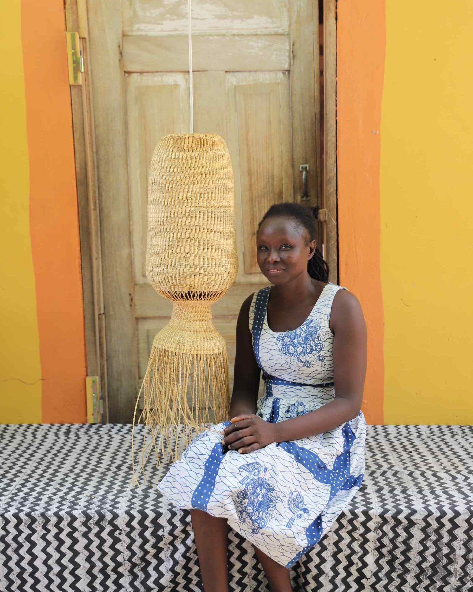 Woman in a patterned dress seated beside the Abyssal lampshade in a weathered doorway.