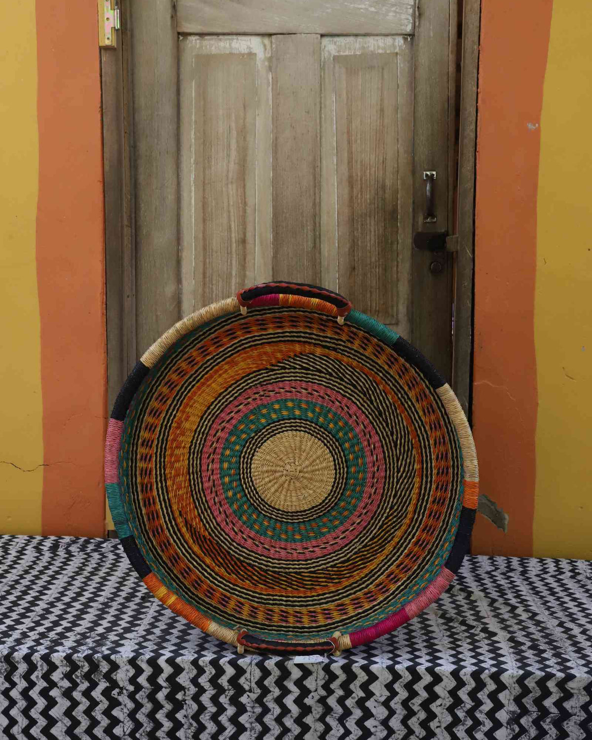 Single-weave handwoven Bolga wall tray disc in bright multicolour concentric bands with dark rim.