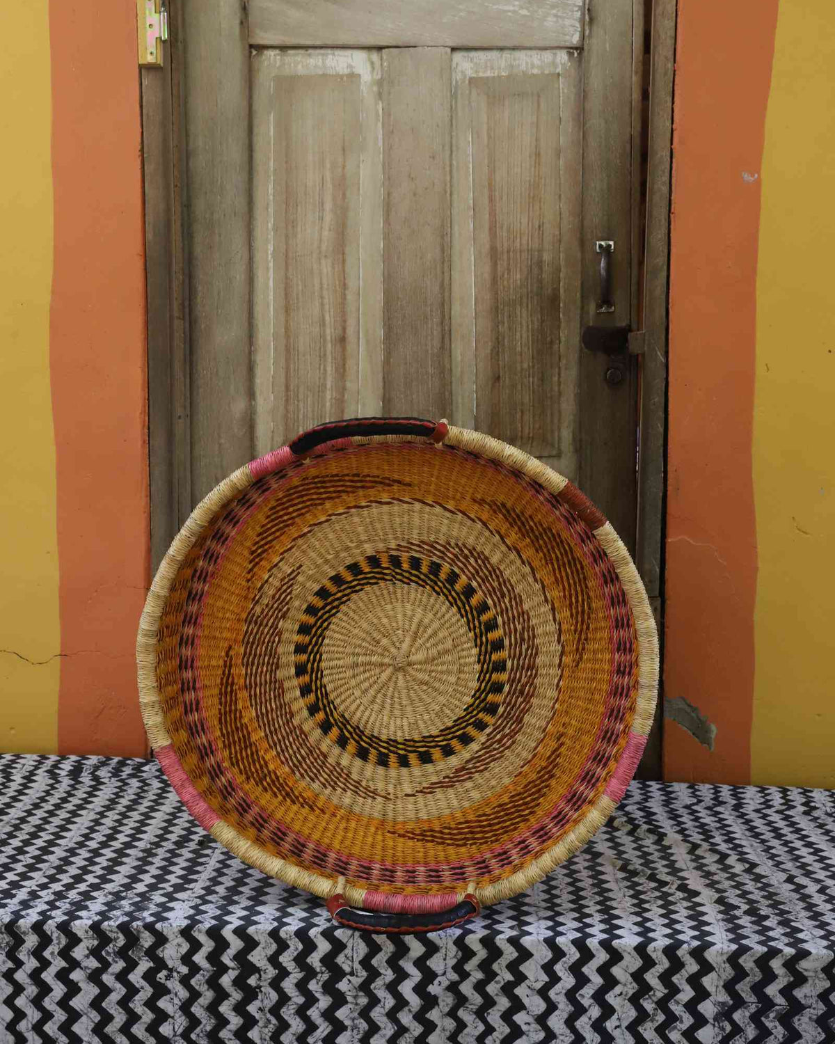 Single-weave handwoven Bolga wall tray disc with orange, red and purple concentric bands and pink handle.