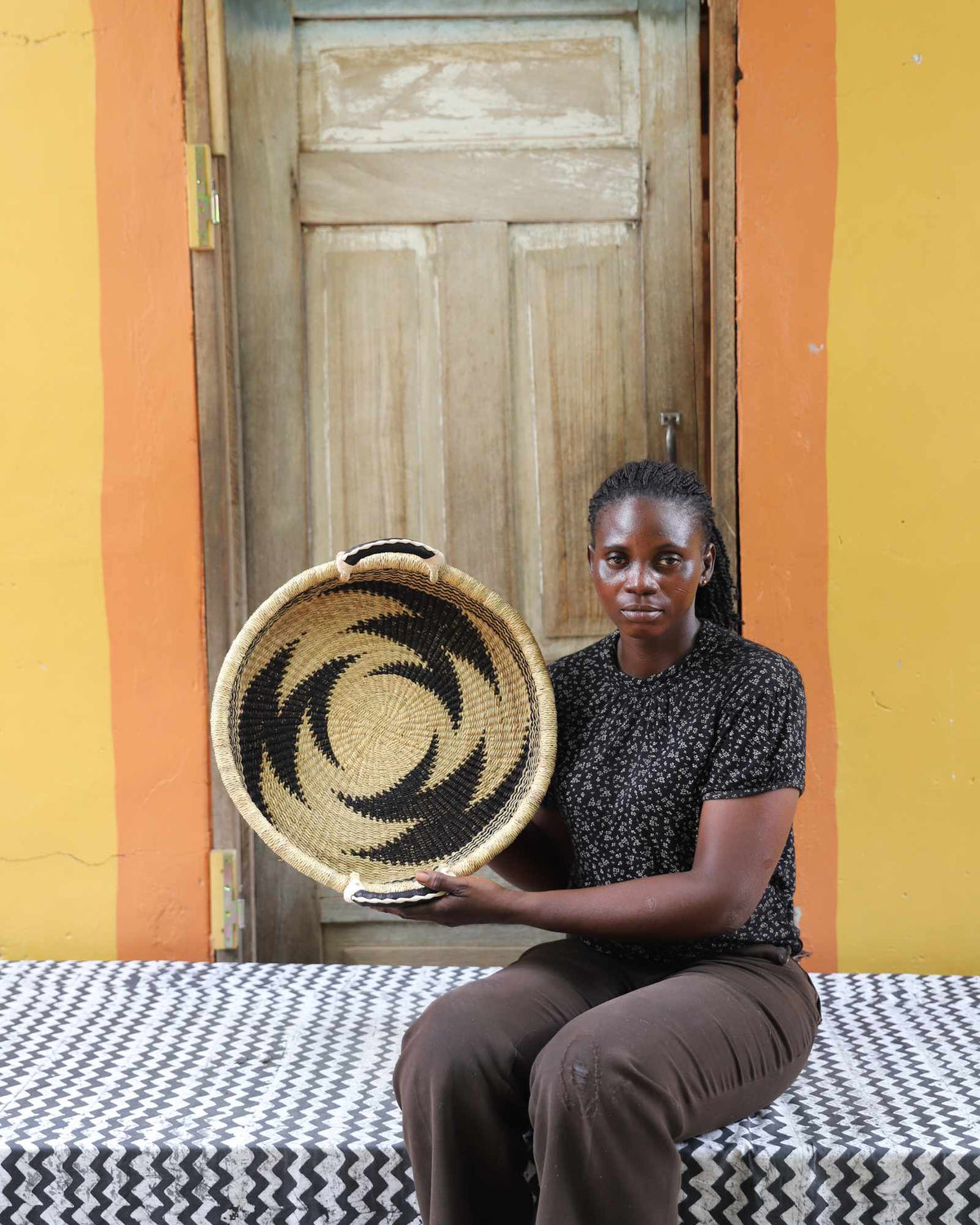 Handwoven Bolga wall tray disc with bold black star pattern, held by a seated woman in dark top.