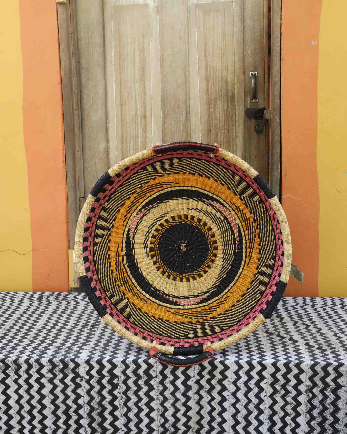 Single-weave handwoven Bolga wall tray disc with orange, black and pink concentric bands and dark centre.