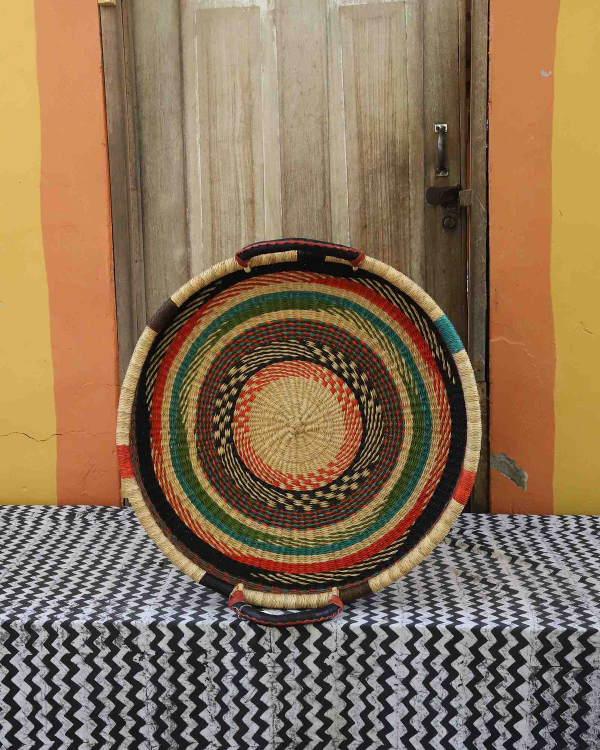 Single-weave handwoven Bolga wall tray disc with red, green and dark concentric bands and yellow centre.