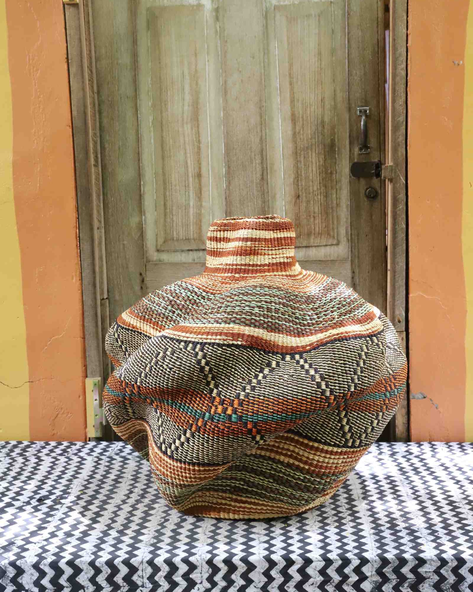 Handwoven African art basket in sculptural lobed vase form with multicoloured earth-tone stripes, on a chevron surface.