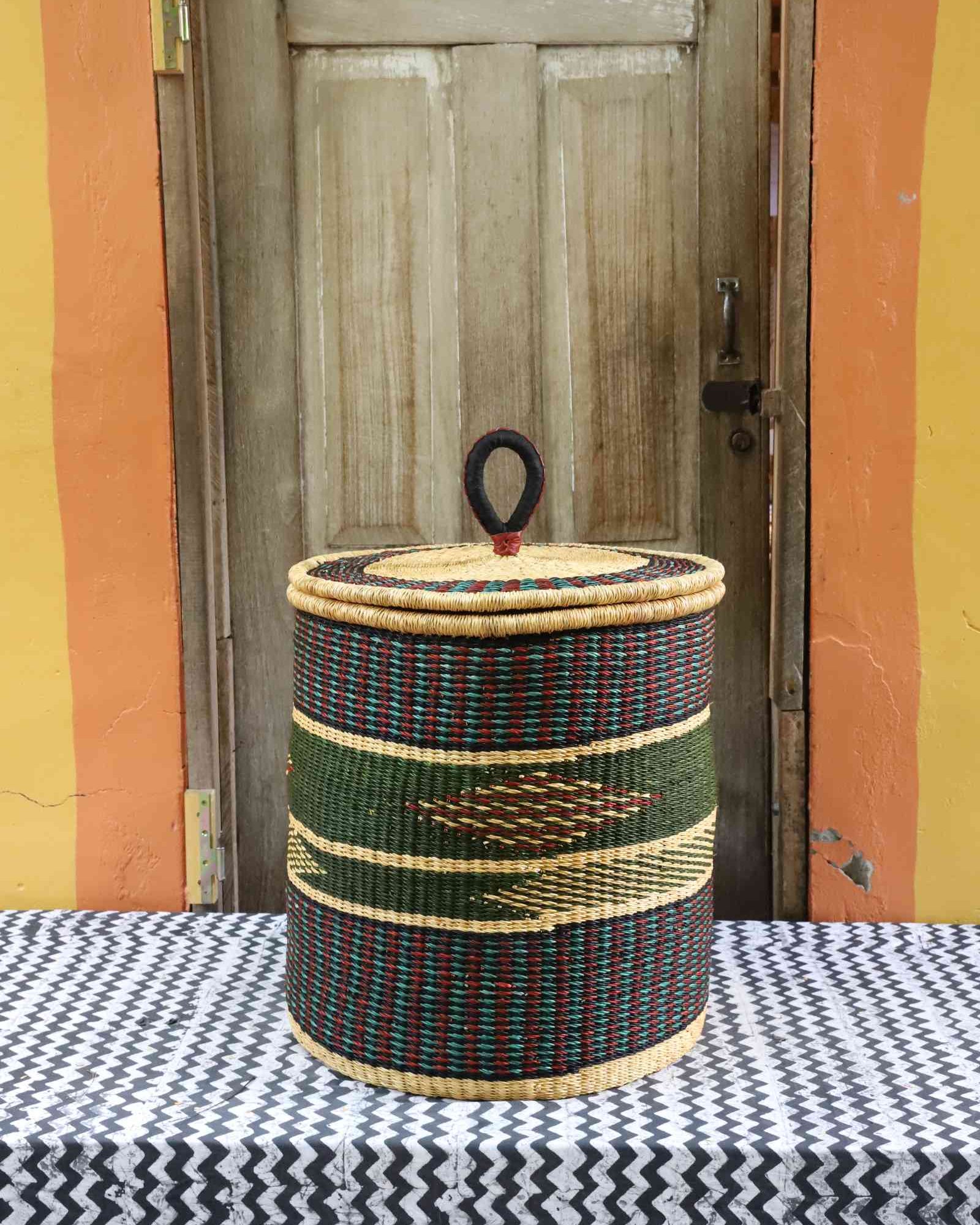 Handwoven Bolga laundry basket with coiled rim and lid in natural straw with a dark green band and arrow motif.