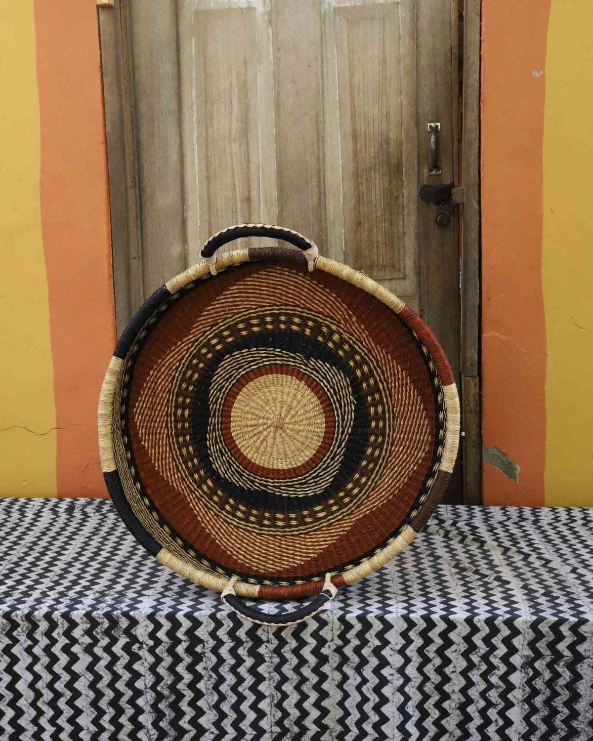 Single-weave handwoven Bolga wall tray disc with brown, red and dark banded rings and natural centre.