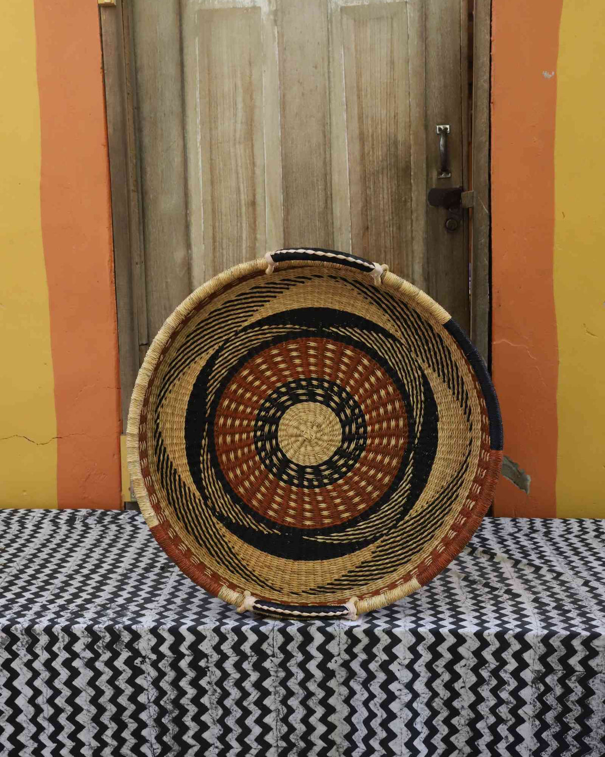 Single-weave handwoven Bolga wall tray disc with orange, black and yellow concentric bands and natural centre.