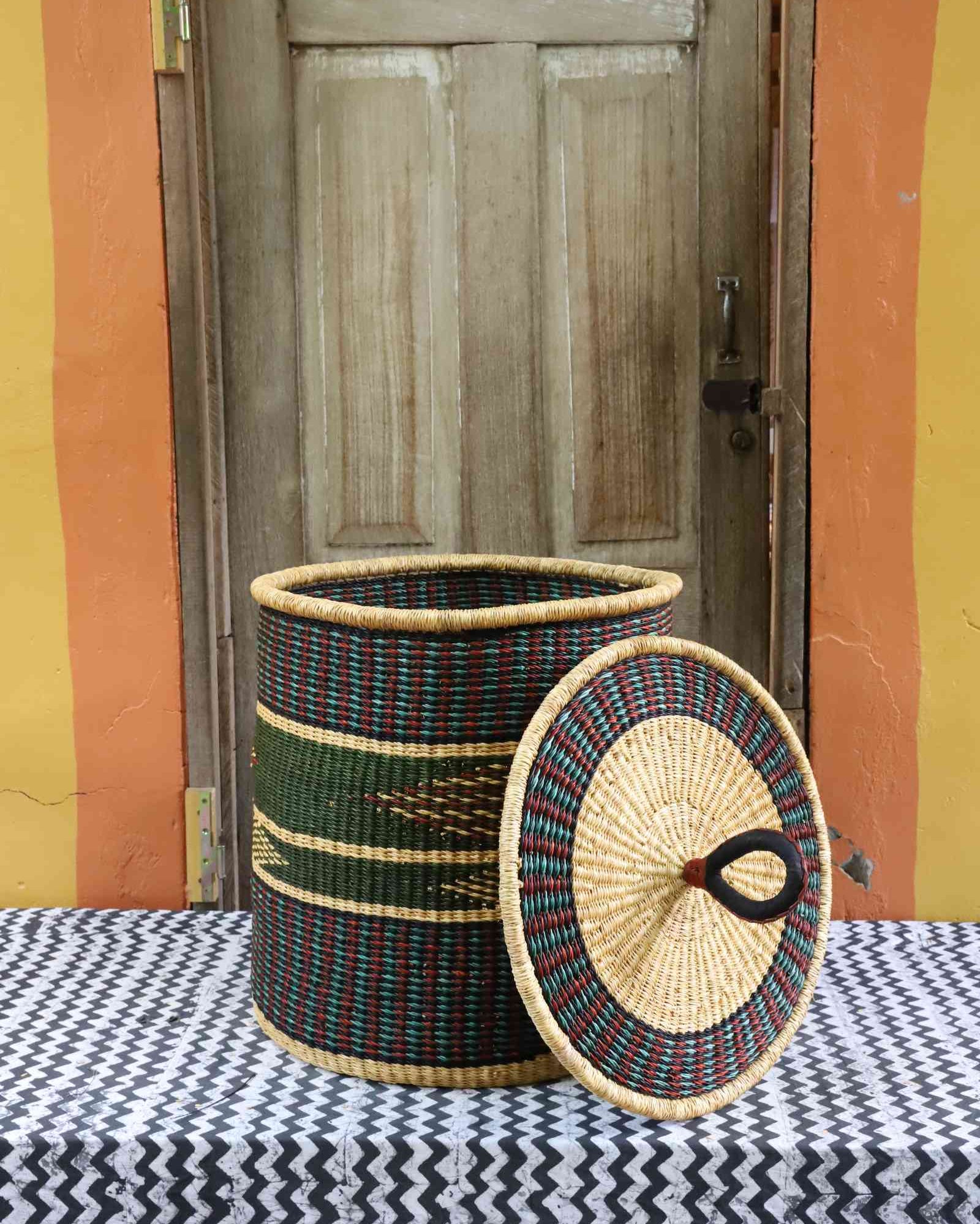 Handwoven Bolga laundry basket with lid removed, natural straw body with dark green band and arrow motif.