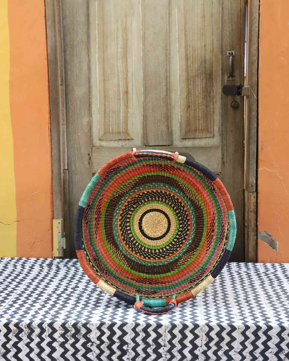 Handwoven Bolga wall tray disc with fine concentric multicolour rings on a dark body.