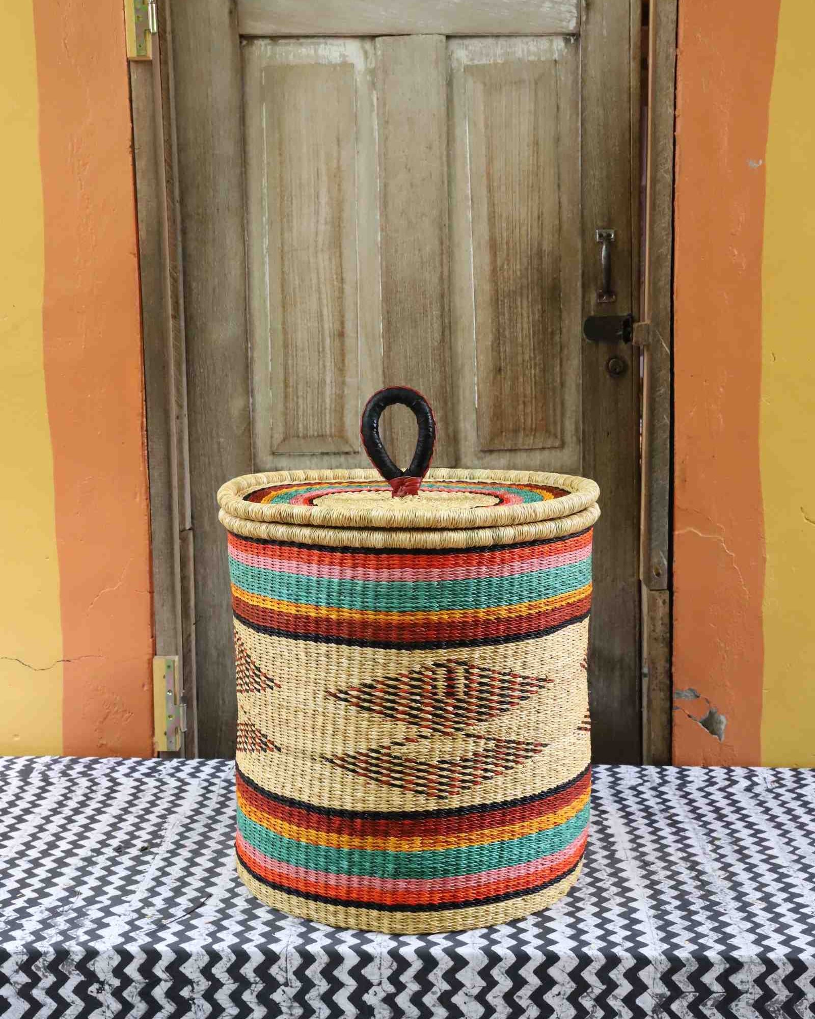 Handwoven Bolga laundry basket with coiled rim and lid in natural straw with fine multicolour bands and central motif.