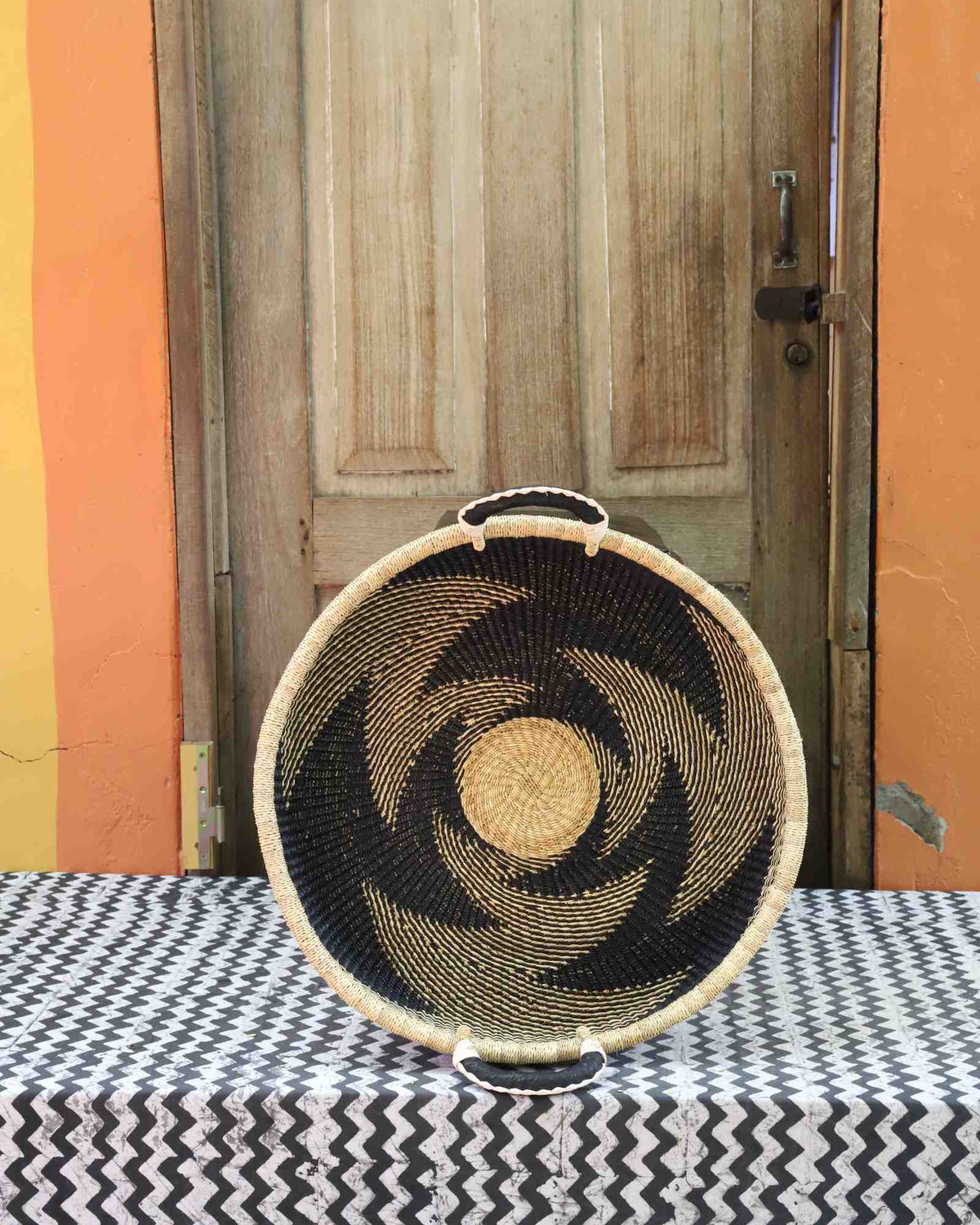 Handwoven Bolga wall tray disc in natural straw with a dark pinwheel swirl pattern.