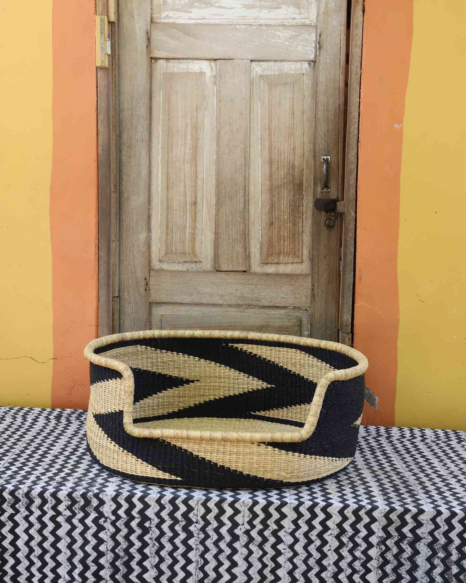 Large handwoven Bolga pet bed in natural straw with a bold black chevron and arrow pattern.