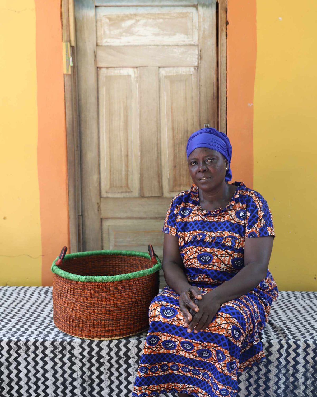 Small handwoven Bolga storage tub in natural straw with a fine green rim, styled beside a seated woman.