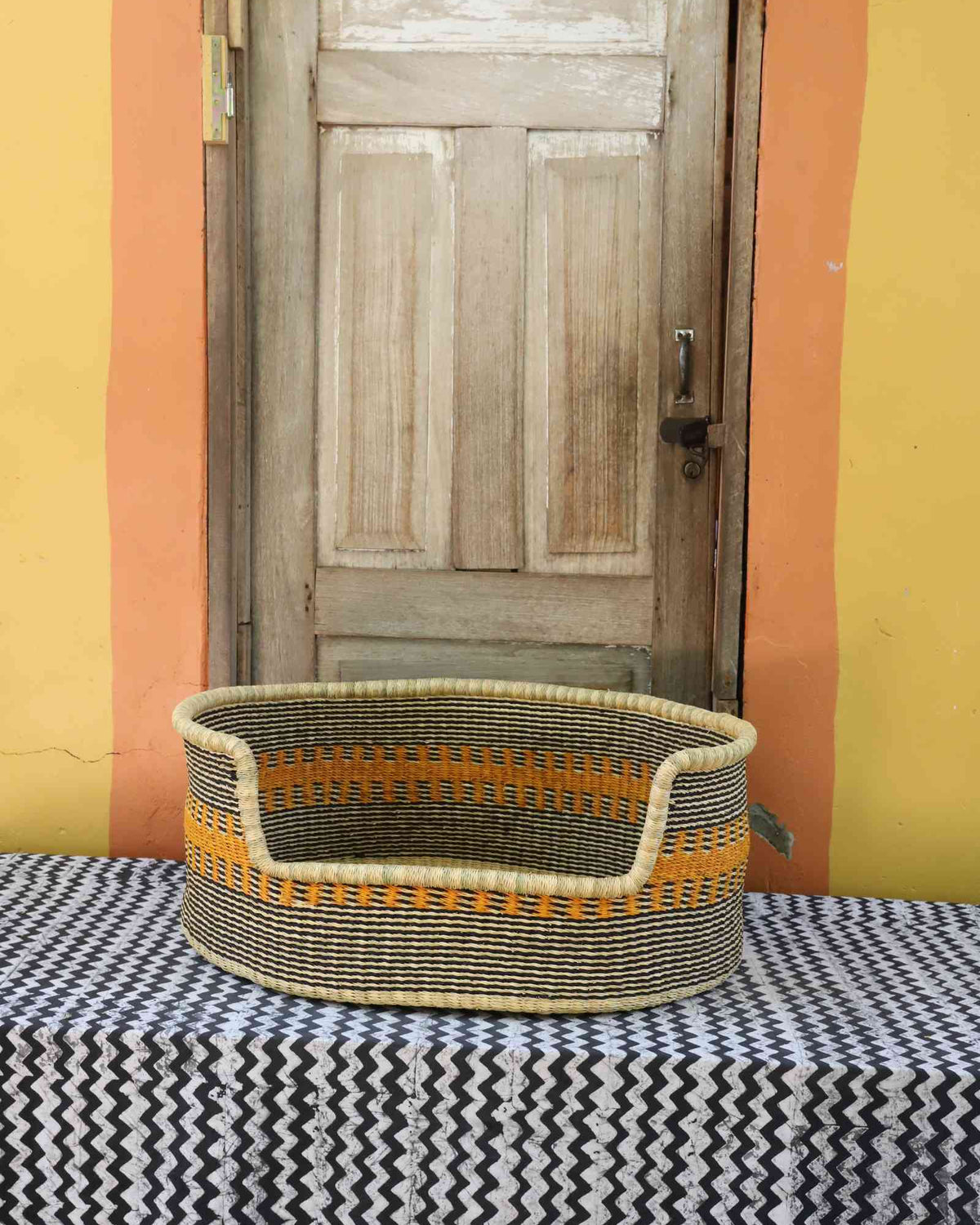 Large handwoven Bolga pet bed in natural straw with a wide orange and yellow banded central stripe.