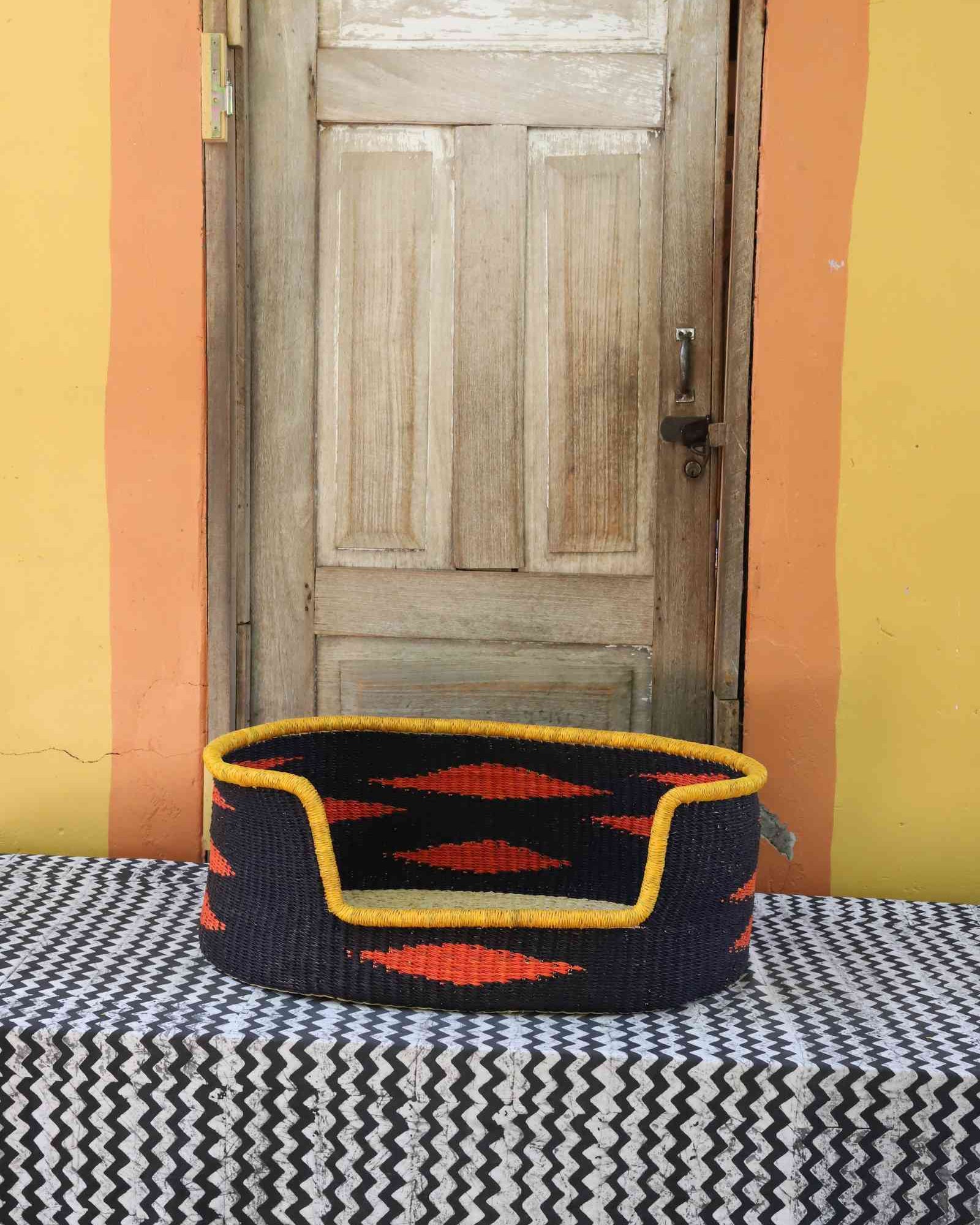 Medium handwoven Bolga pet bed in bold black with orange diamond flames and a yellow banded rim.