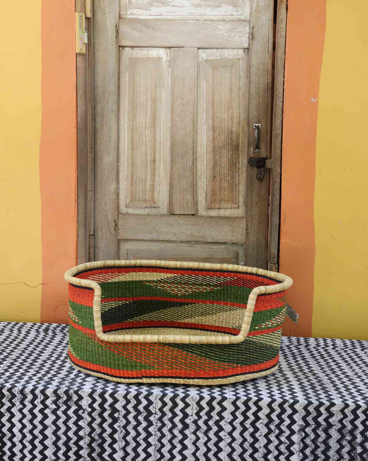 Large handwoven Bolga pet bed in natural straw with green, red and orange horizontal banded stripes.