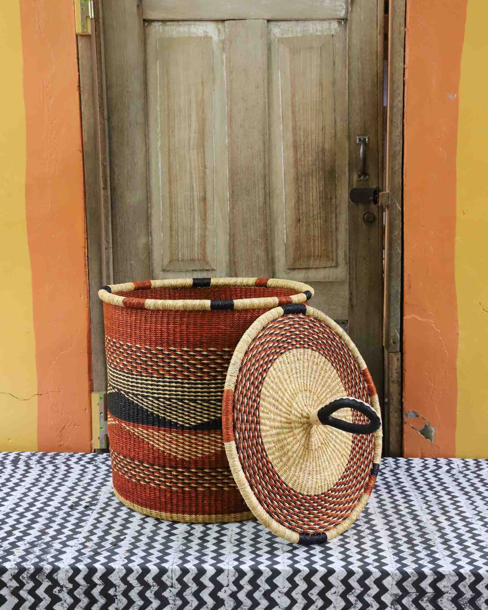 Handwoven Bolga laundry basket with lid removed, rust-orange body with dark wave motif and matching lid.