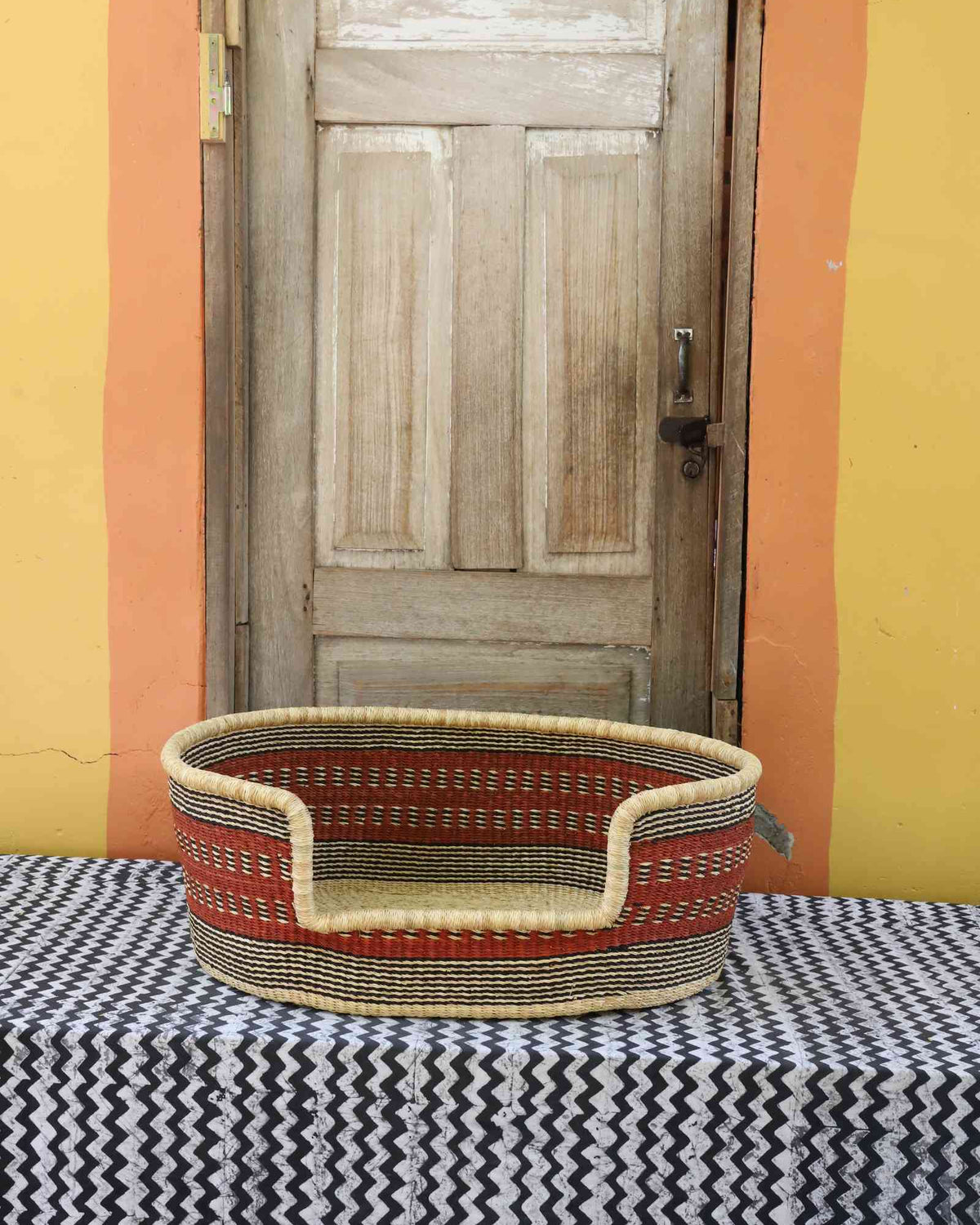 Medium handwoven Bolga pet bed in natural straw with red horizontal banded stripes.